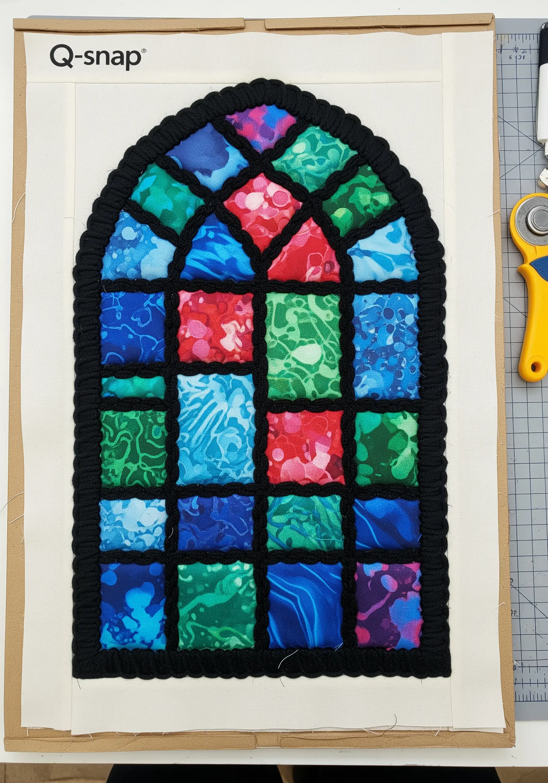 A fabric collage that looks like a stained glass window, with black yarn for leading.
