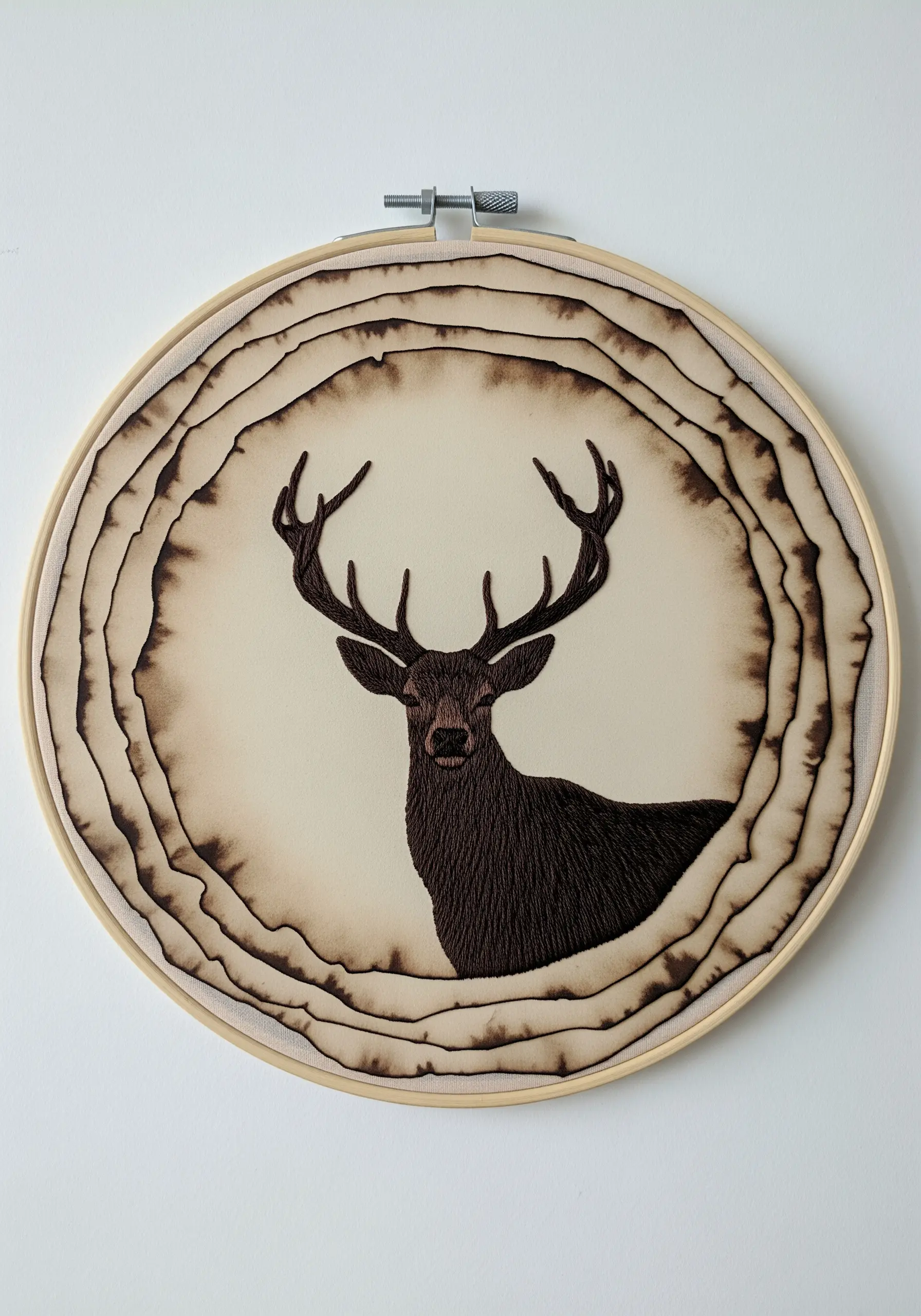 A deer silhouette embroidered in dark brown thread, framed by painted rings that resemble tree rings.
