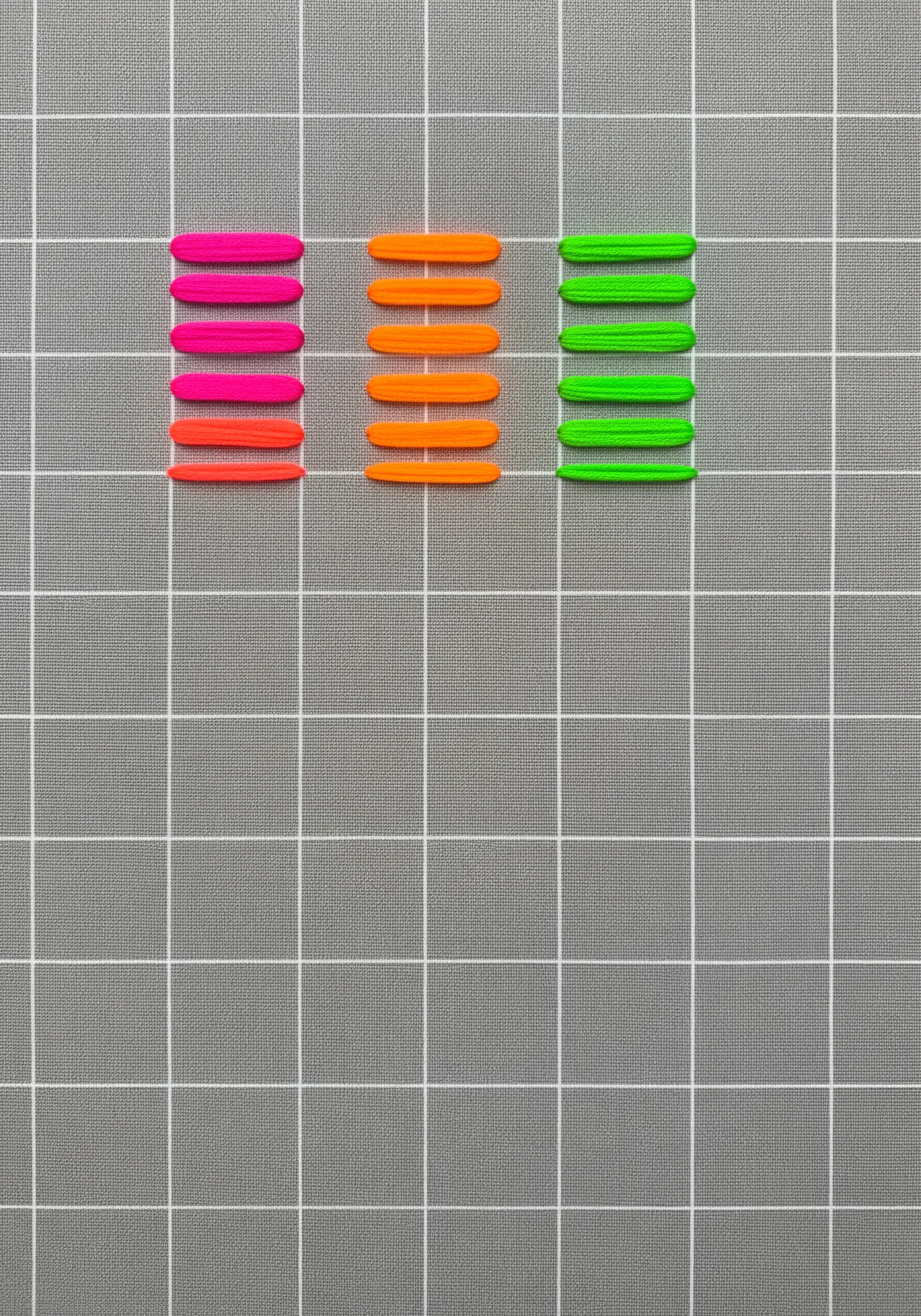 Three columns of neon satin stitch blocks on a gray gridded fabric.