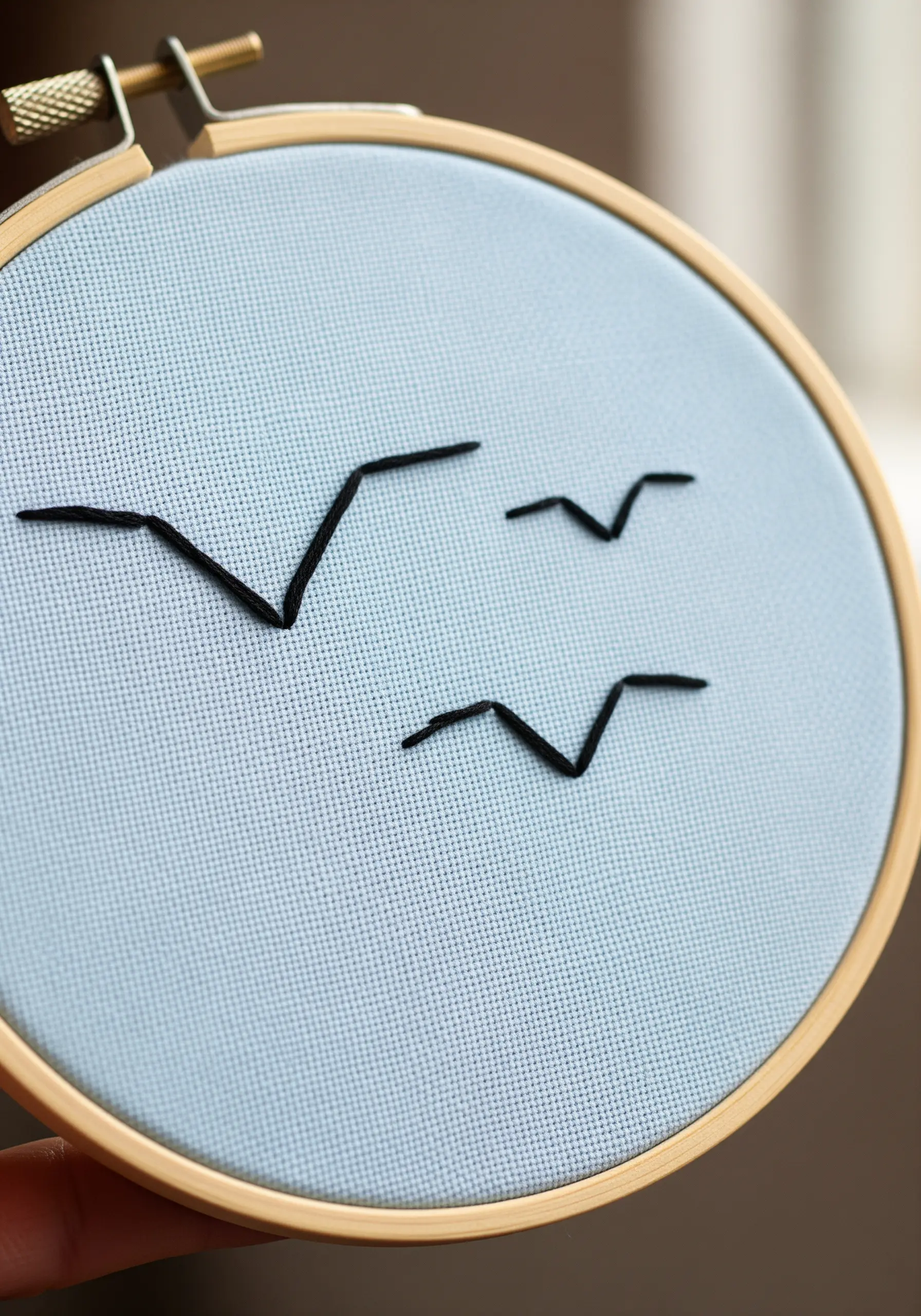 Three simple black bird silhouettes in flight, embroidered on light blue fabric.