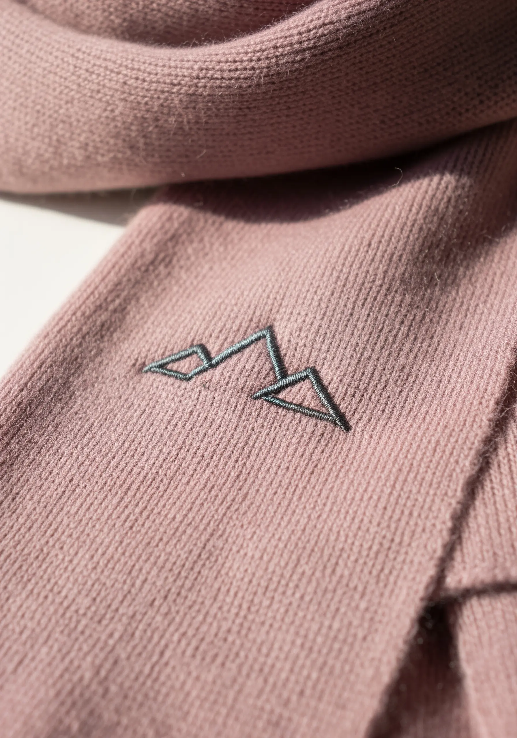A minimalist outline of a mountain range with subtle fill stitching on a pink scarf.