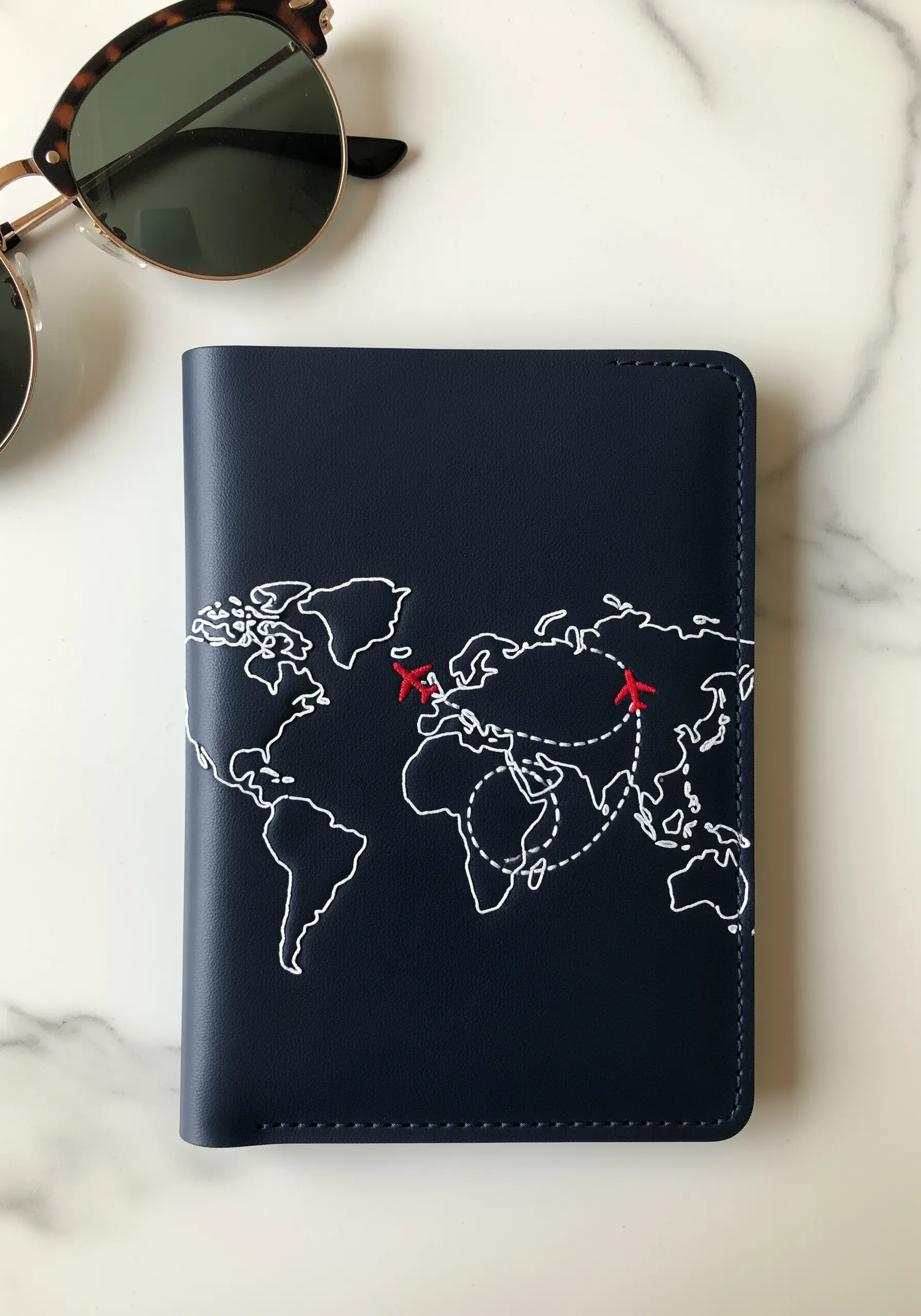 A navy passport cover with a minimalist world map outlined in white backstitch and red details.