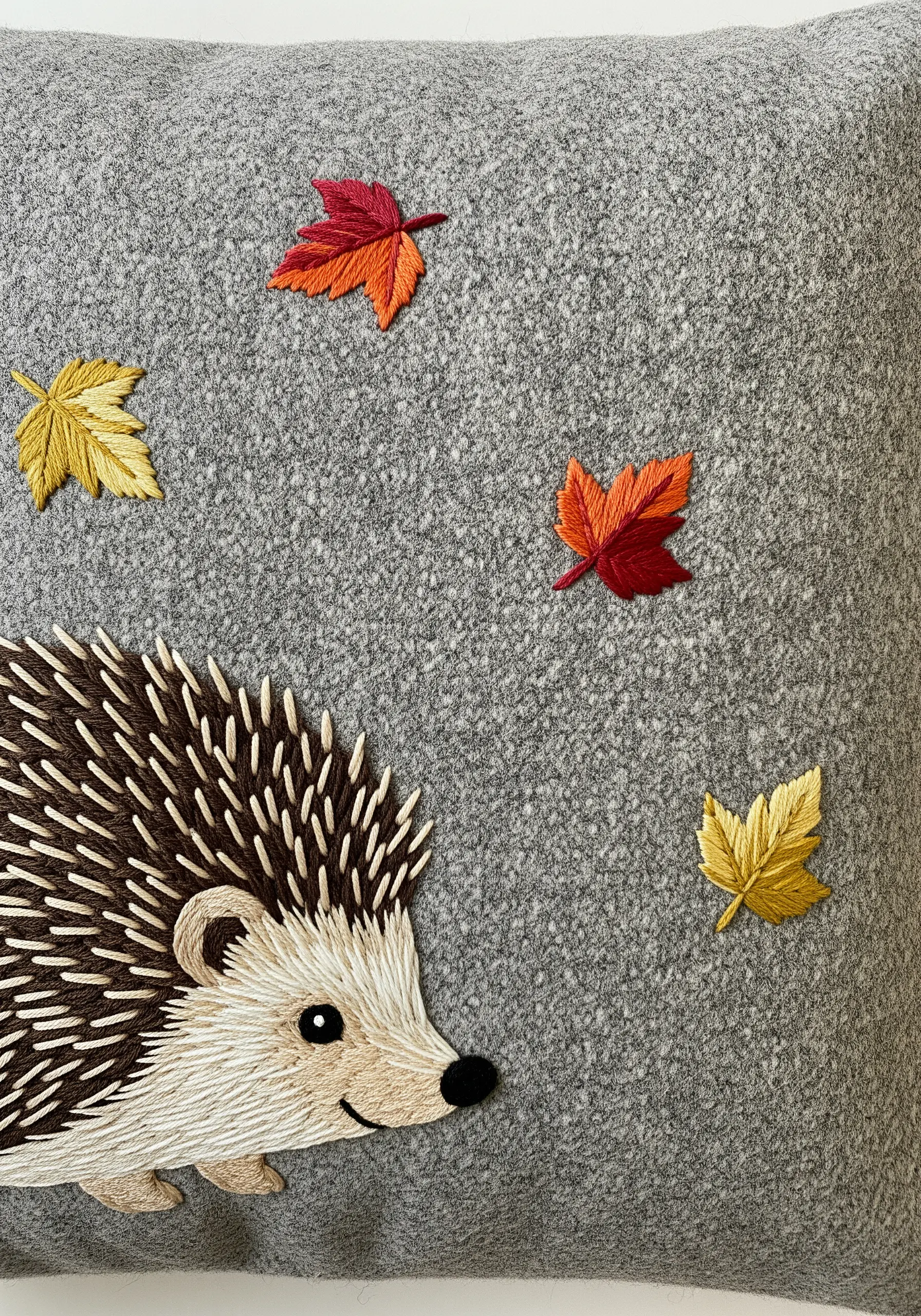 Embroidered hedgehog with straight-stitch spines and satin-stitched autumn leaves.