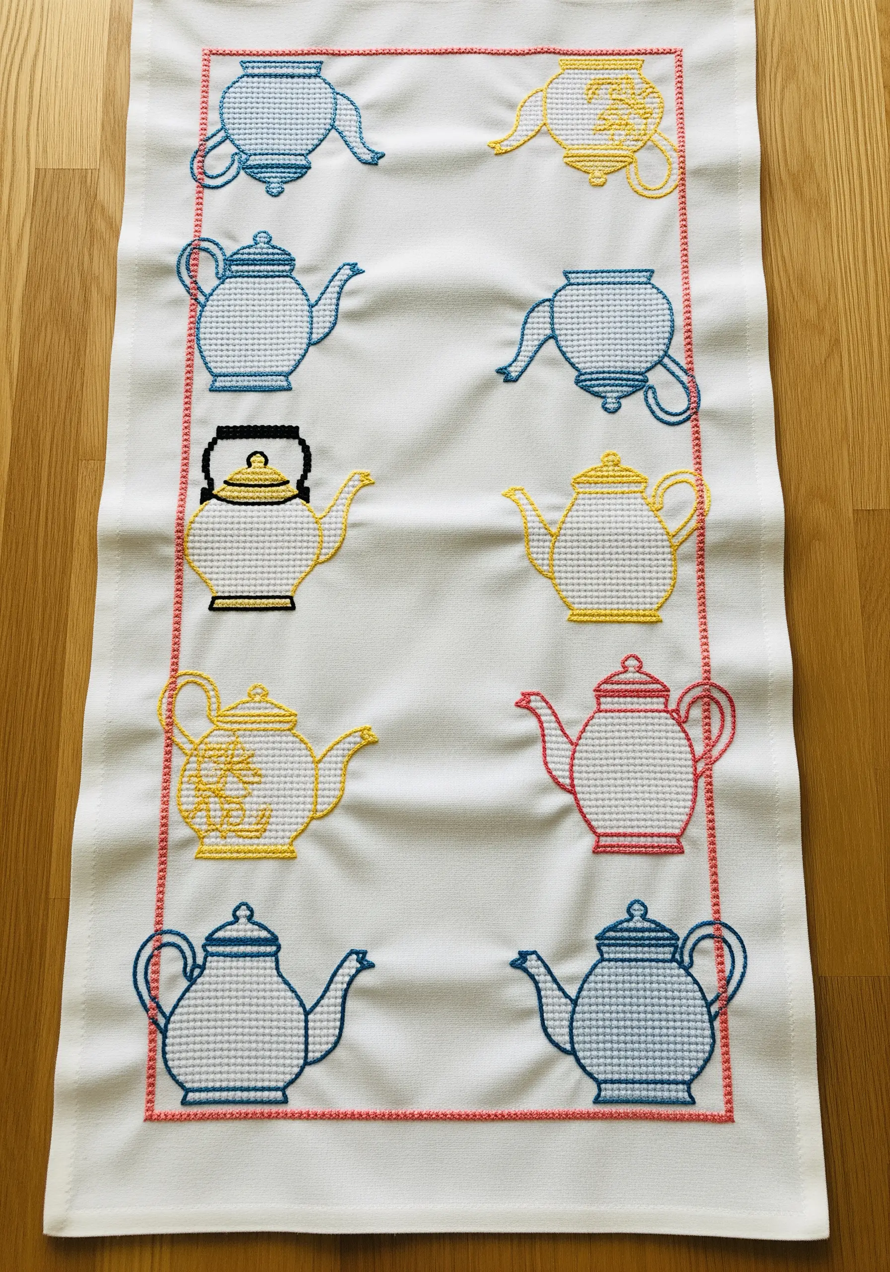 A collection of cross-stitched teapot motifs in a grid on a table runner.