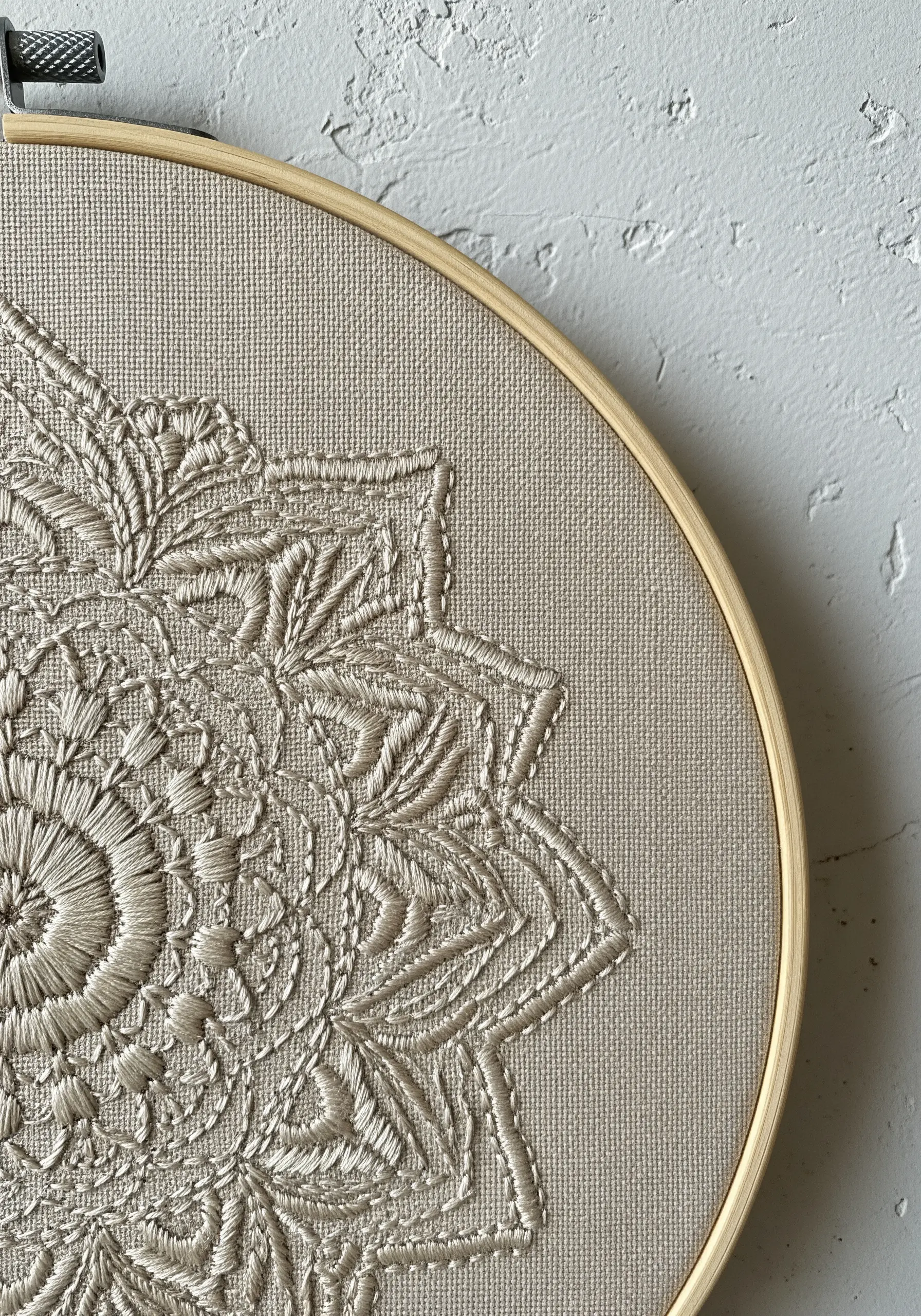 A close-up of a monochromatic mandala on beige fabric, showcasing a variety of stitch textures.
