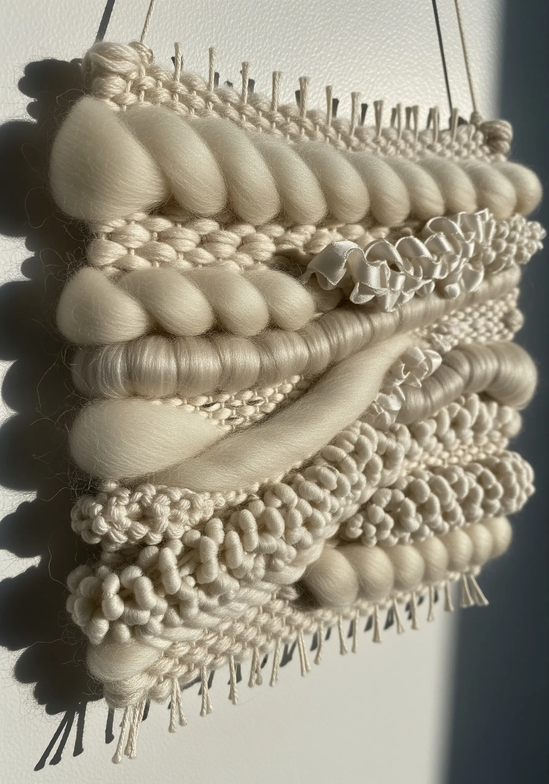 A highly textured, all-white woven wall hanging with various knots, braids, and loops.