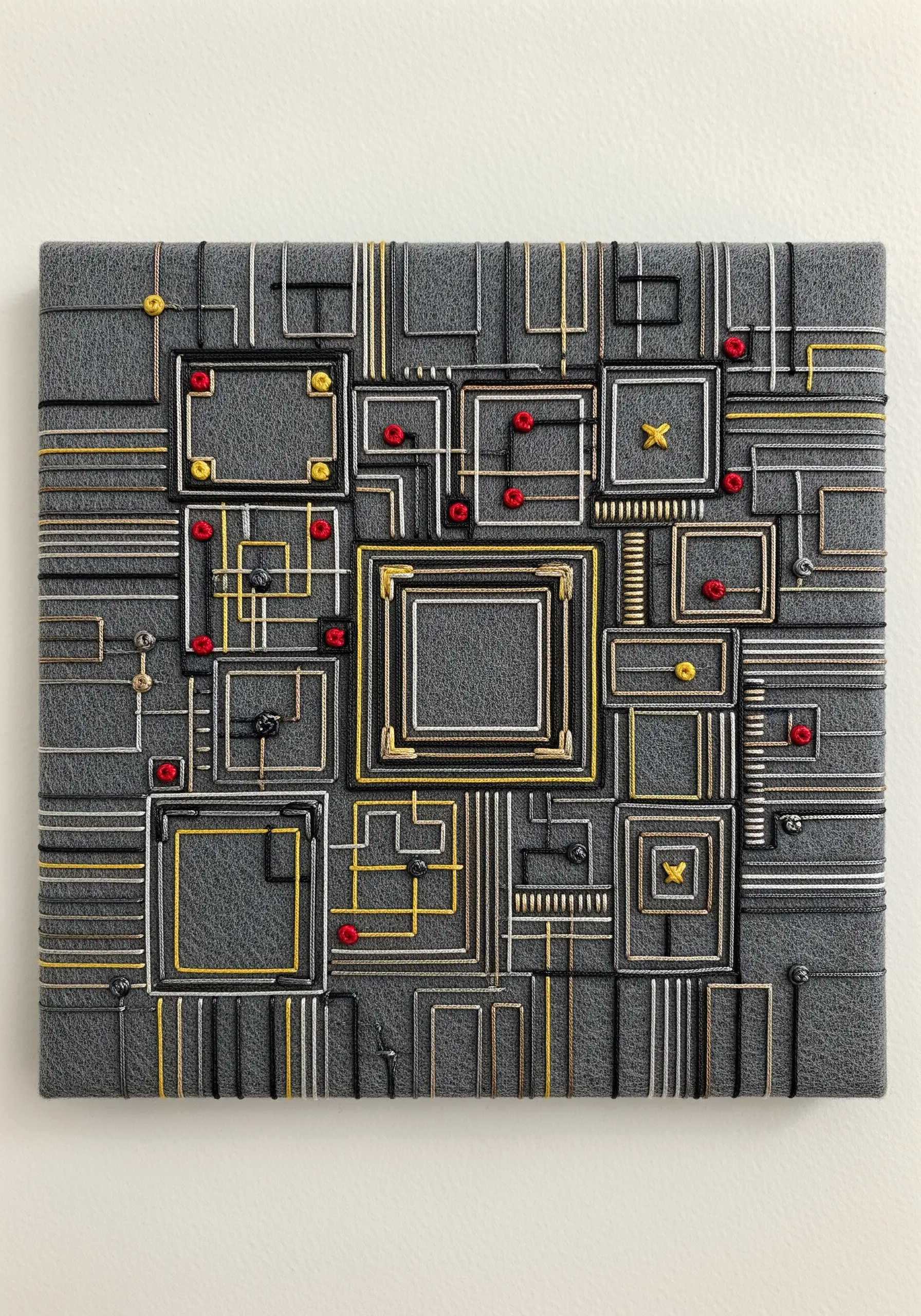 A complex, multi-layered circuit board embroidery on gray felt with metallic and colored threads.