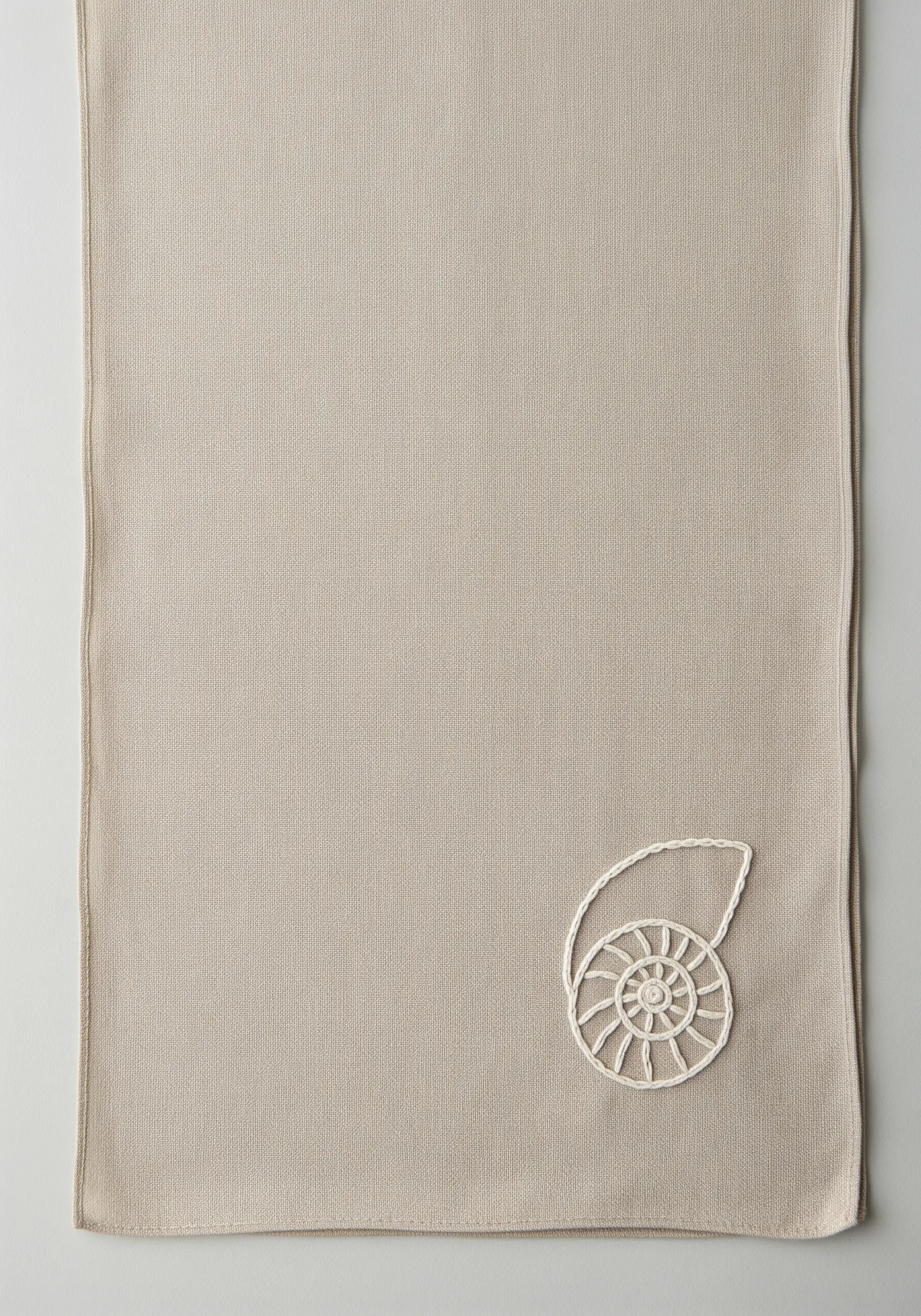 An embroidered nautilus shell with a textured, rope-like outline on a beige scarf.