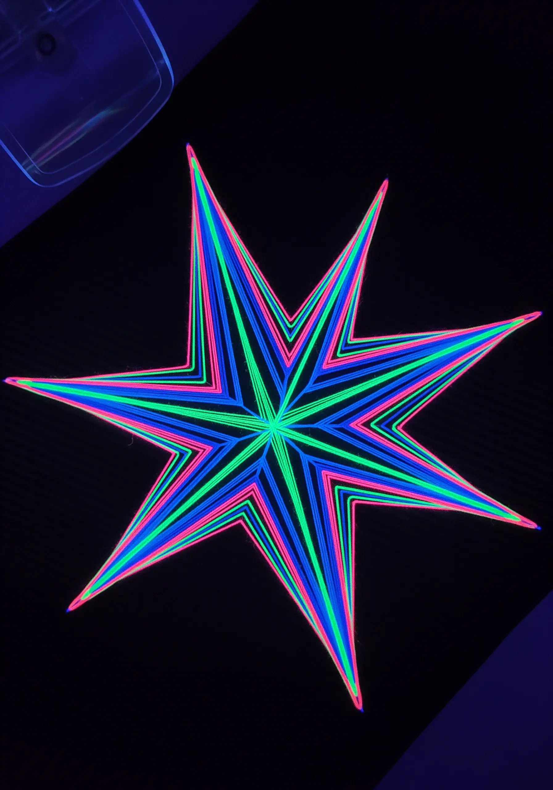 Neon string art star with layered pink, blue, and green thread on a black background.