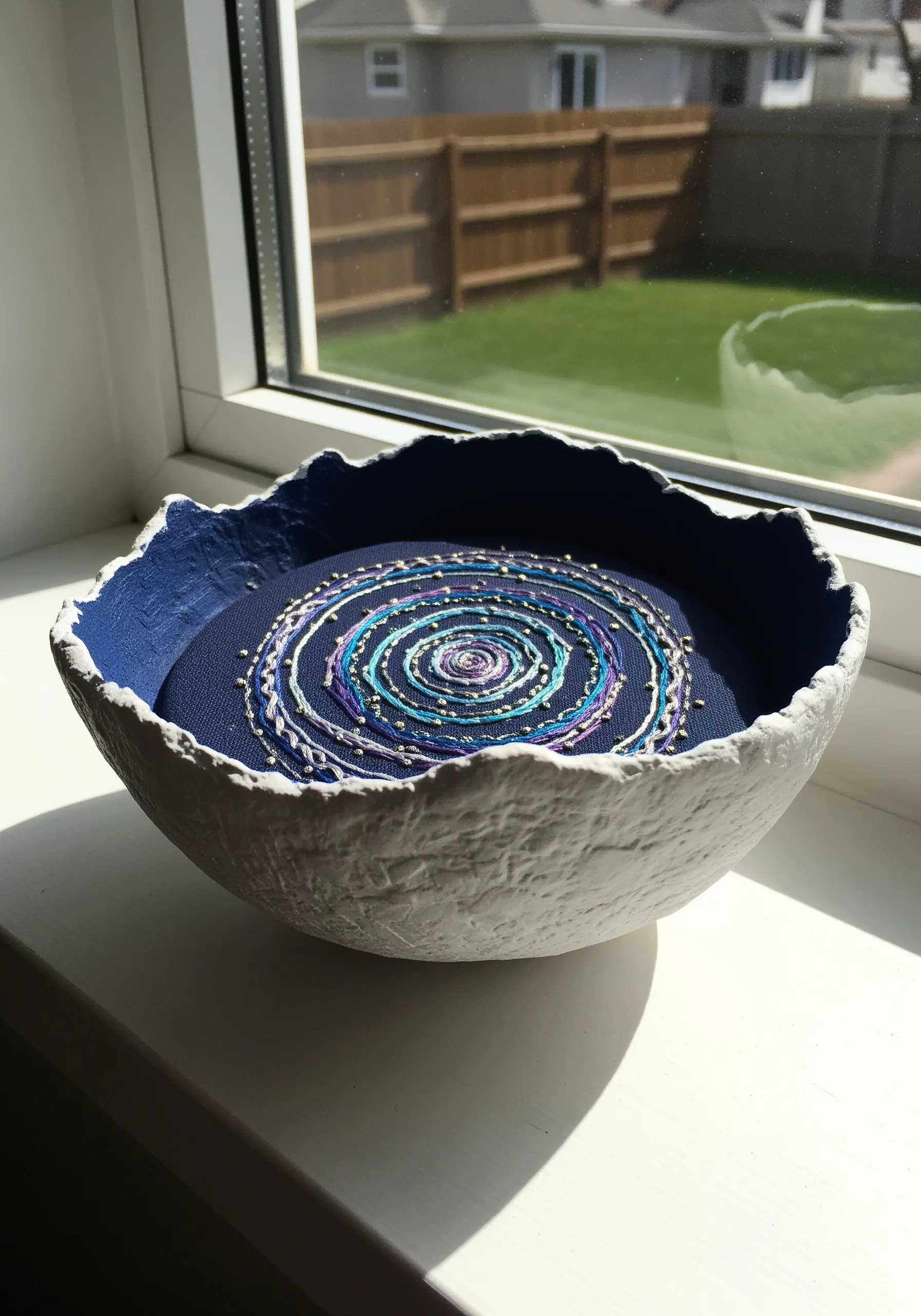 Cosmic swirl embroidery with metallic threads nestled inside a textured paper pulp bowl.