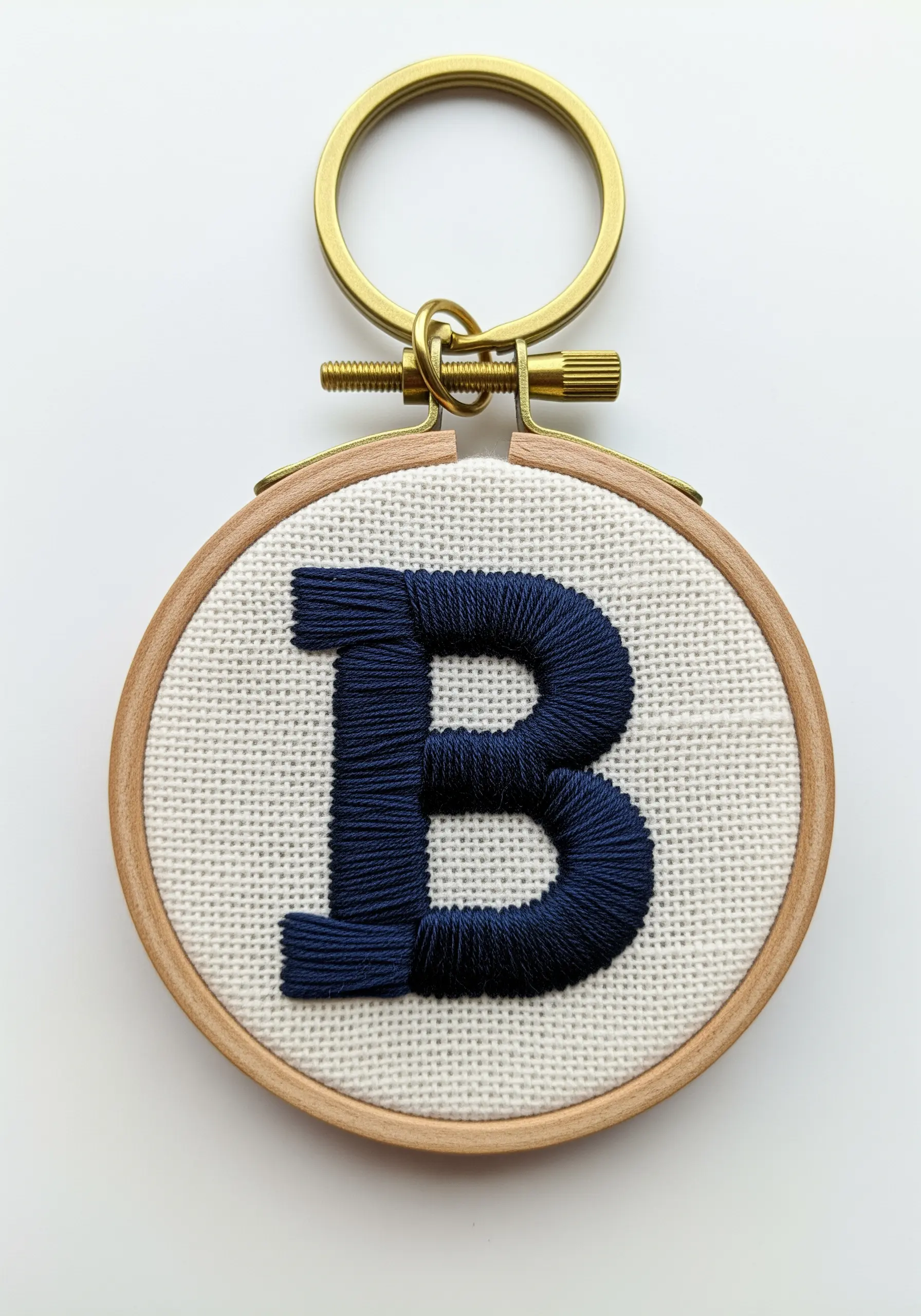 A navy blue satin-stitched letter 'B' in a tiny embroidery hoop keychain