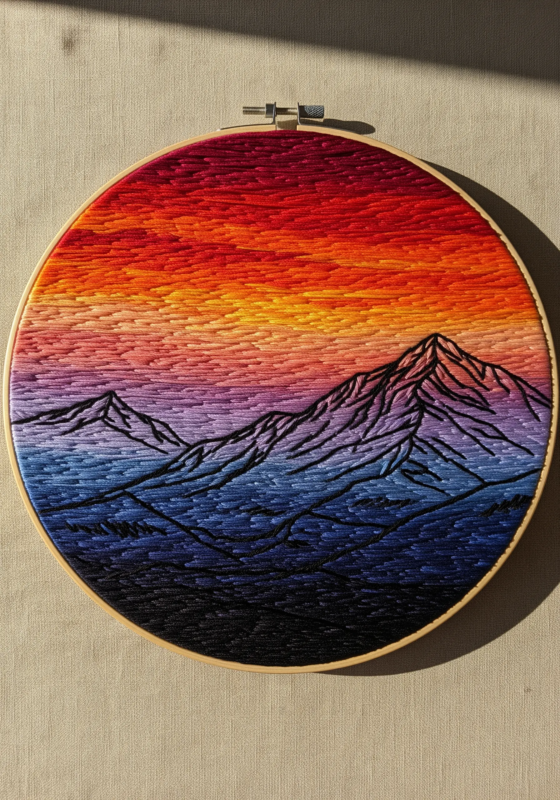 Embroidered sunset landscape with variegated thread and black mountain outlines.