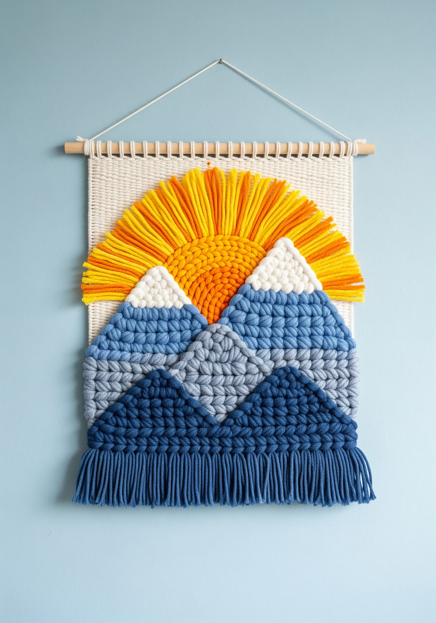 A woven wall hanging depicting a sun rising over blue and grey mountains.