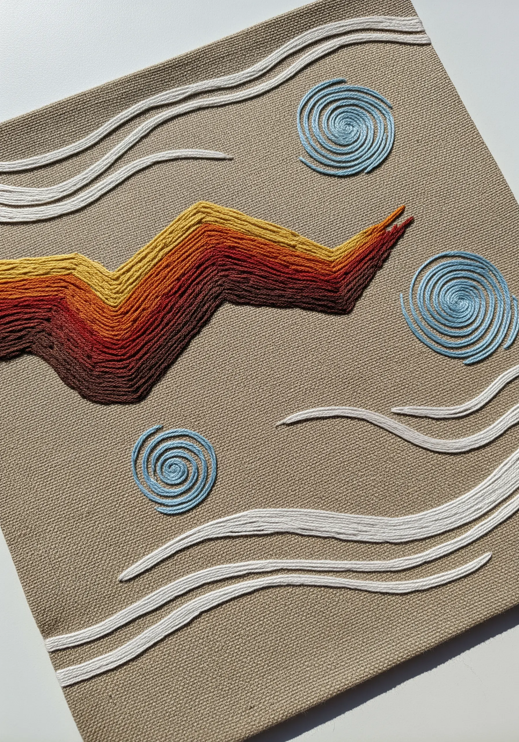 Abstract landscape embroidery with a gradient satin stitch mountain range and blue spiral clouds.