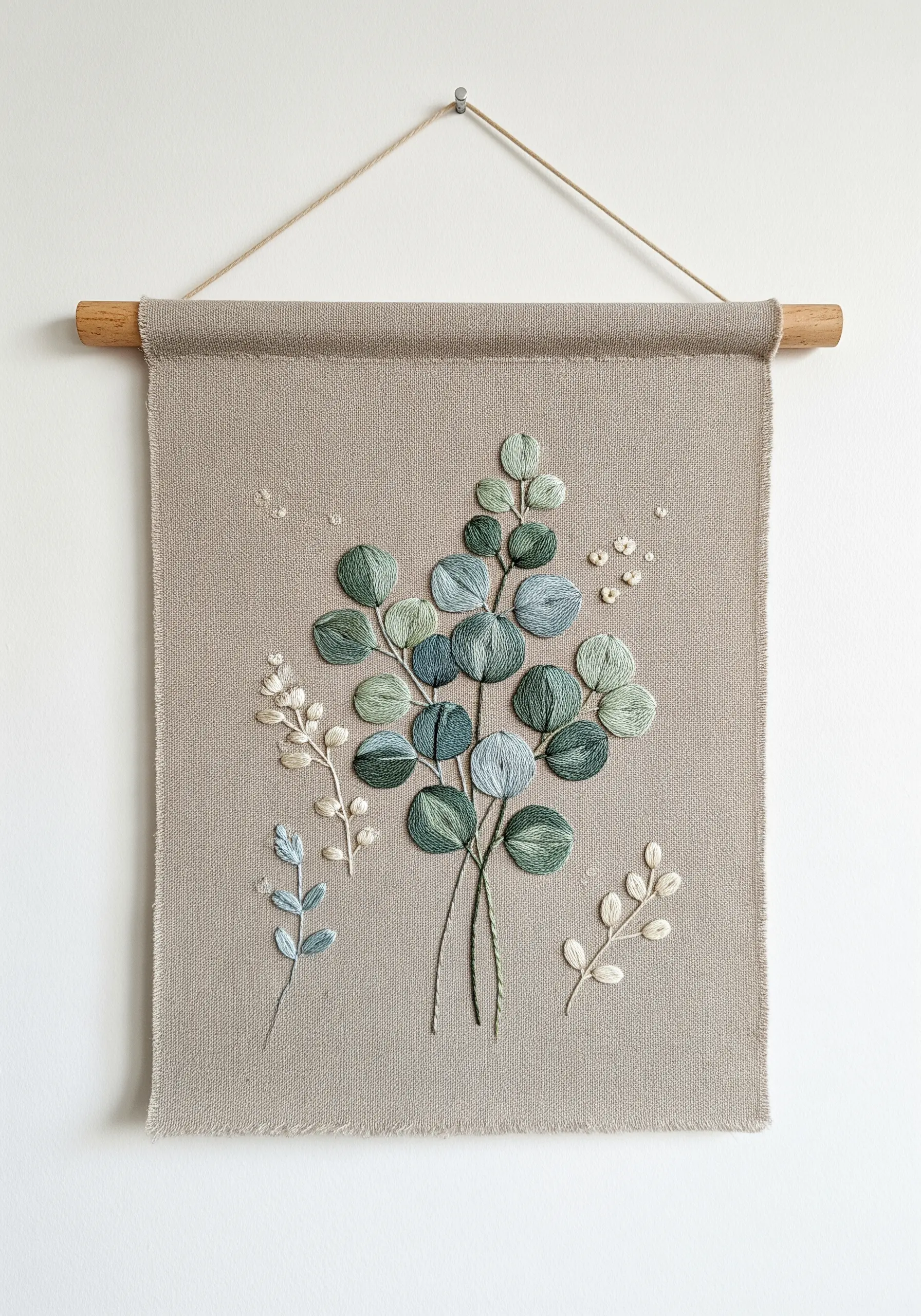 Eucalyptus bouquet embroidered on a linen wall hanging with soft green and blue threads.