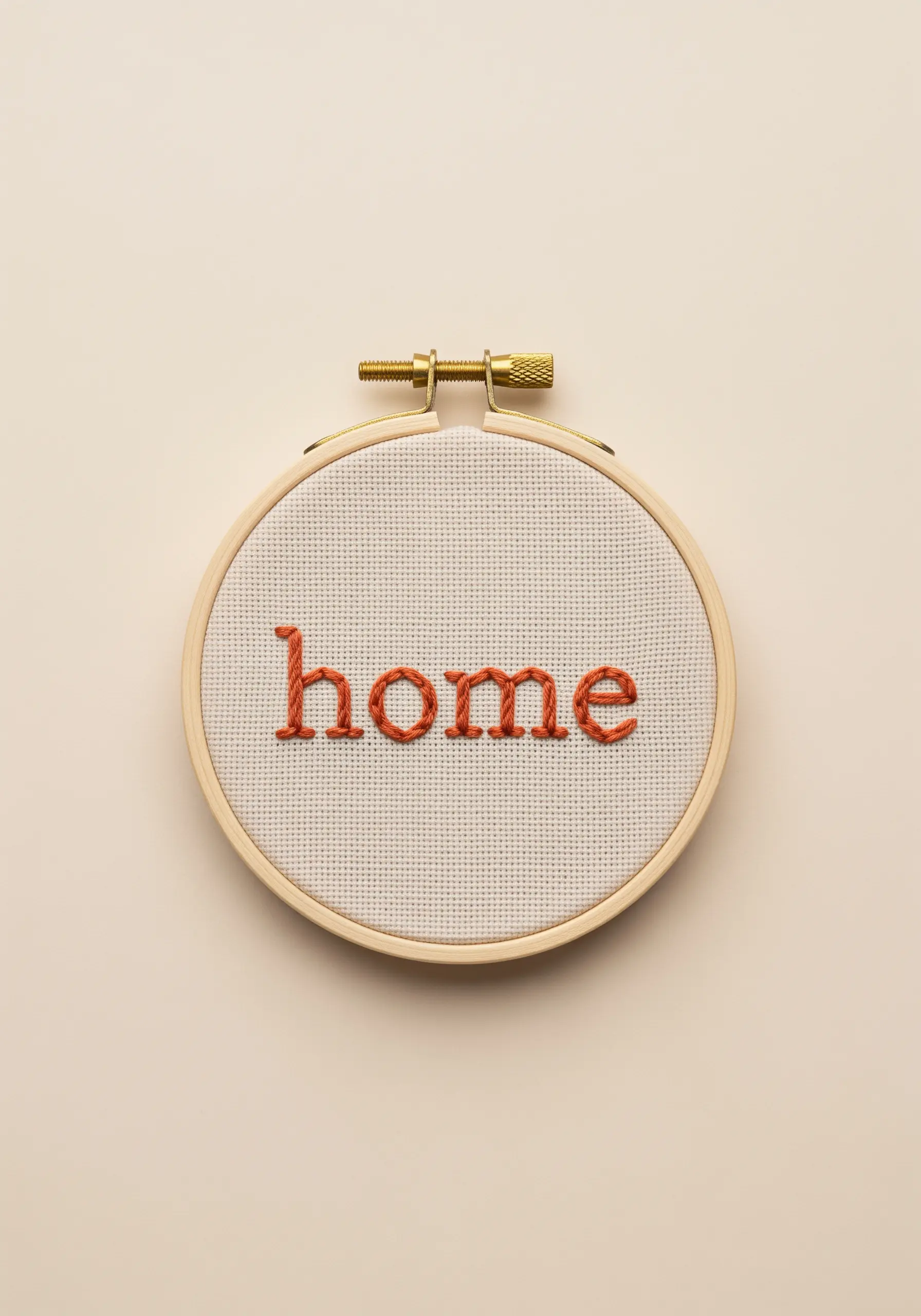 The word 'home' in terracotta stem stitch on white Aida cloth in a hoop.