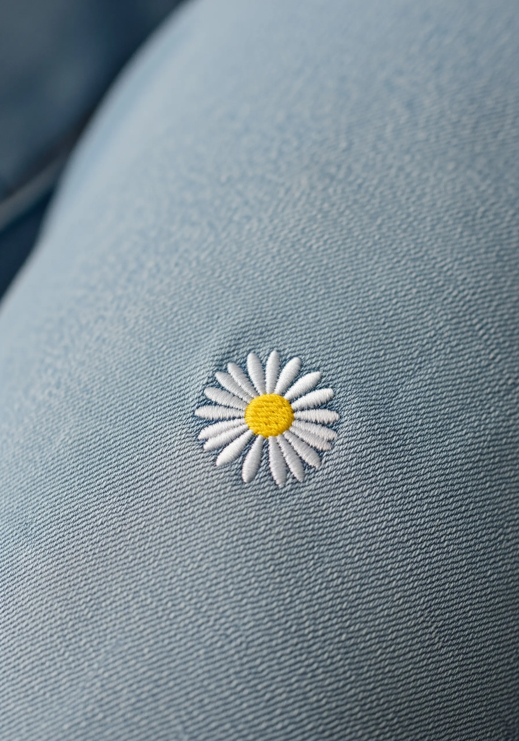 A small, perfect daisy with white petals and a yellow center embroidered on light blue denim.