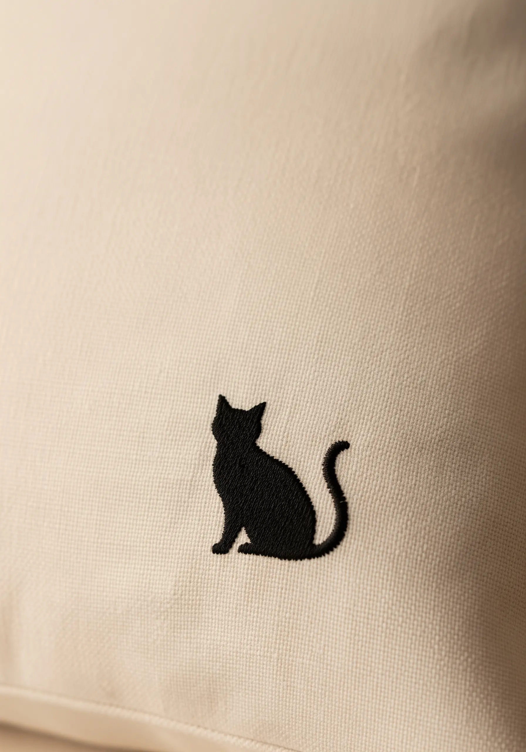 A solid black cat silhouette embroidered with a dense satin stitch on a cream cushion.