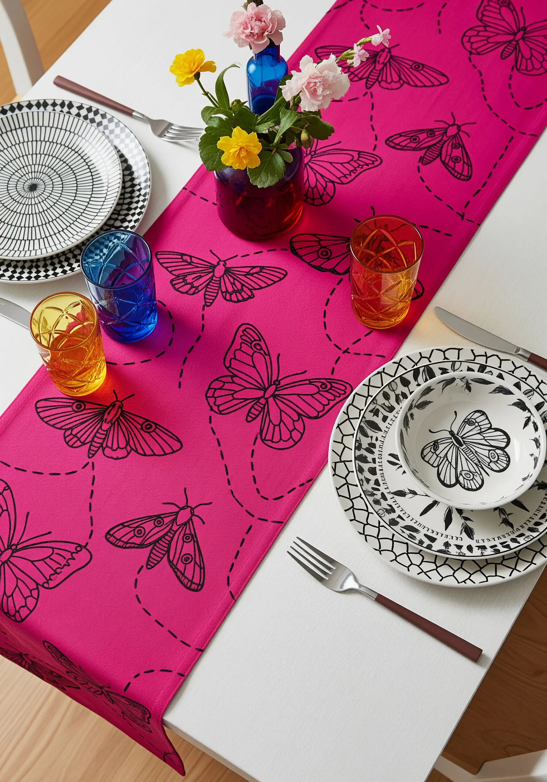 Black outline embroidery of butterflies and moths with dashed flight paths on a fuchsia runner.