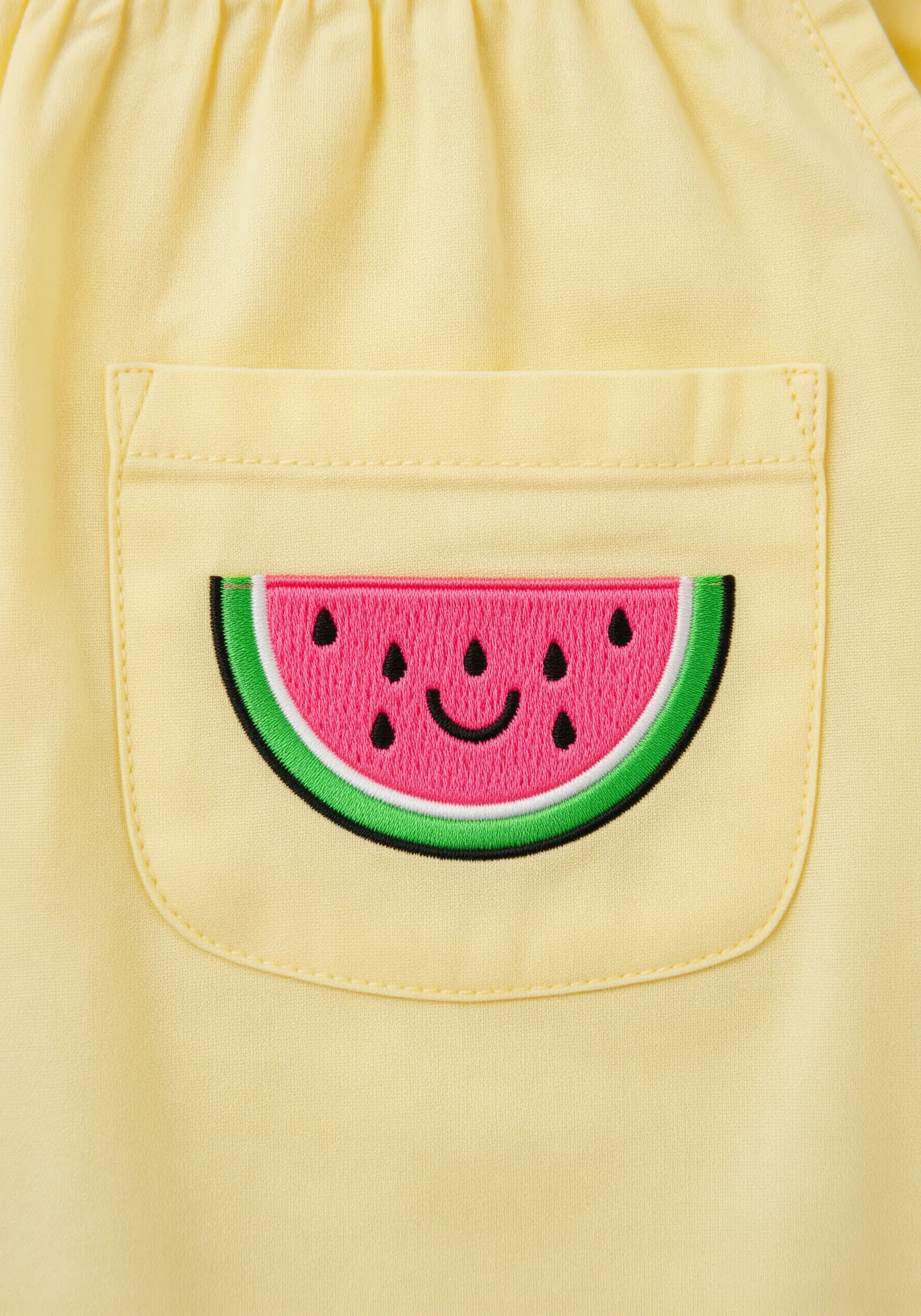 A cheerful embroidered watermelon slice on the pocket of a yellow garment.