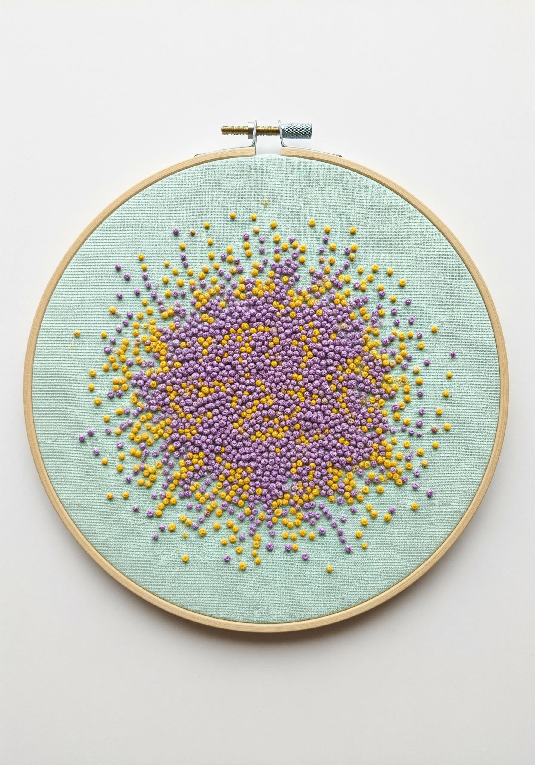 A dense cluster of yellow and purple French knots on a mint green fabric background.