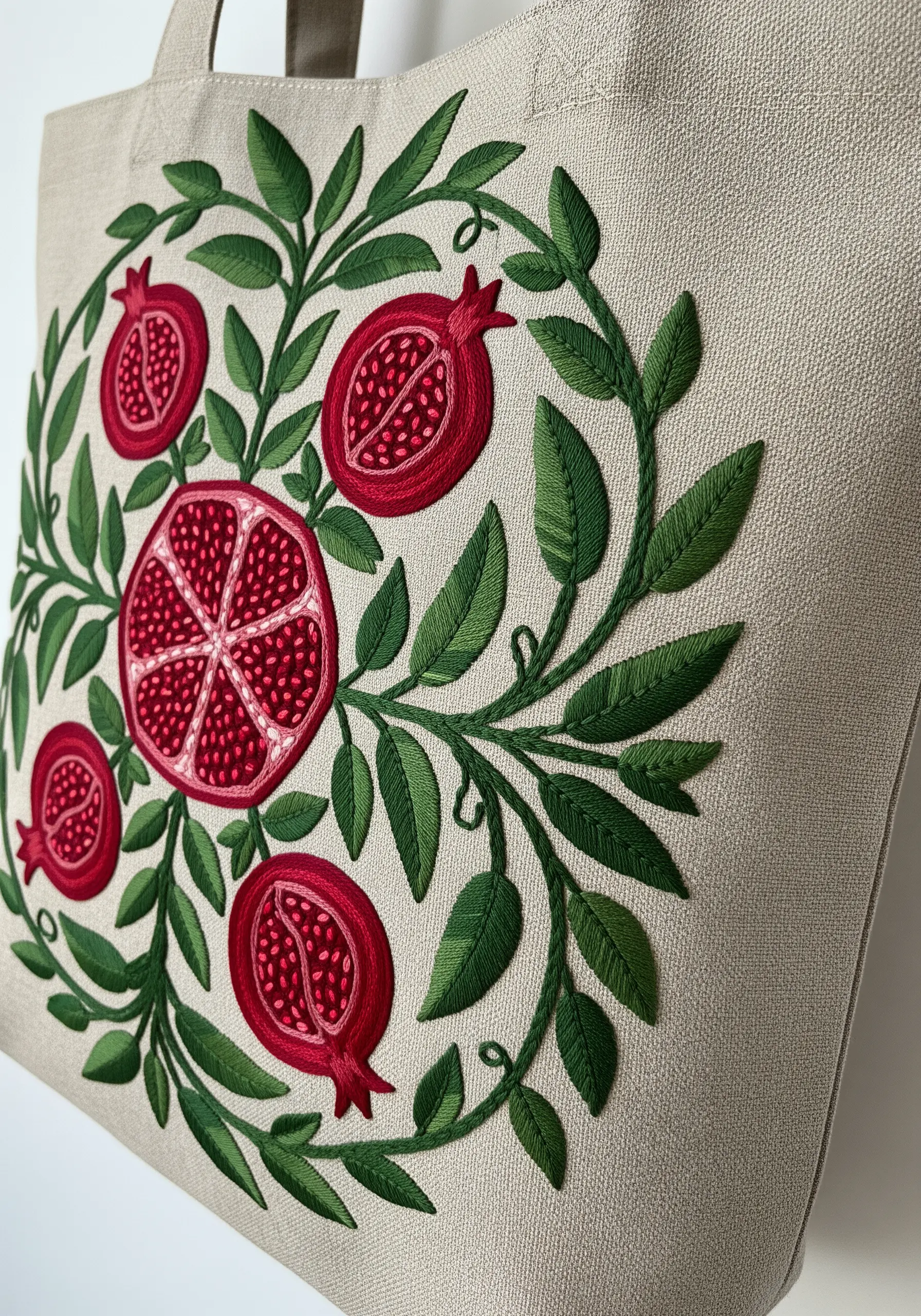 A circular design of pomegranates and leafy vines embroidered on a natural linen tote bag.