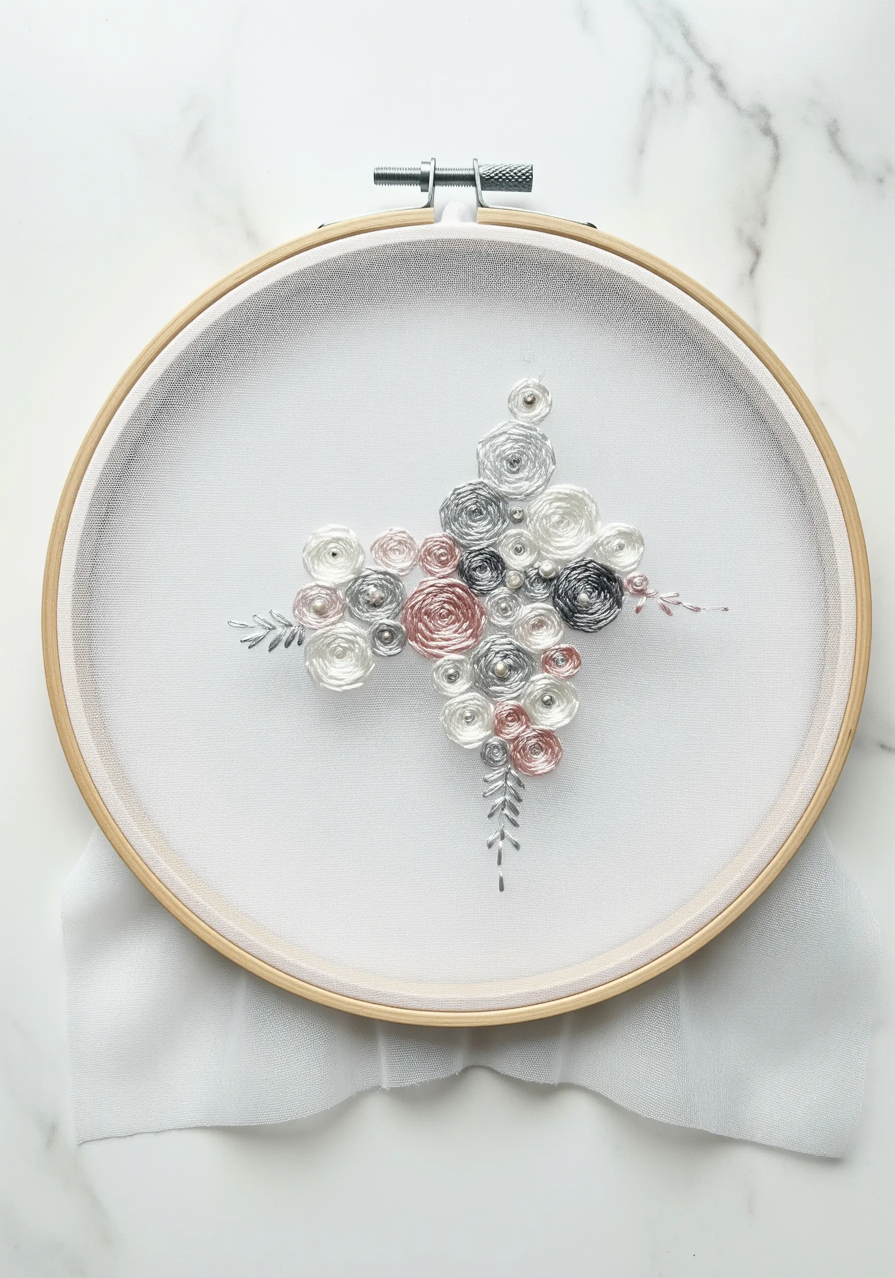 A delicate cluster of woven wheel roses in silver, grey, and pink on sheer fabric.