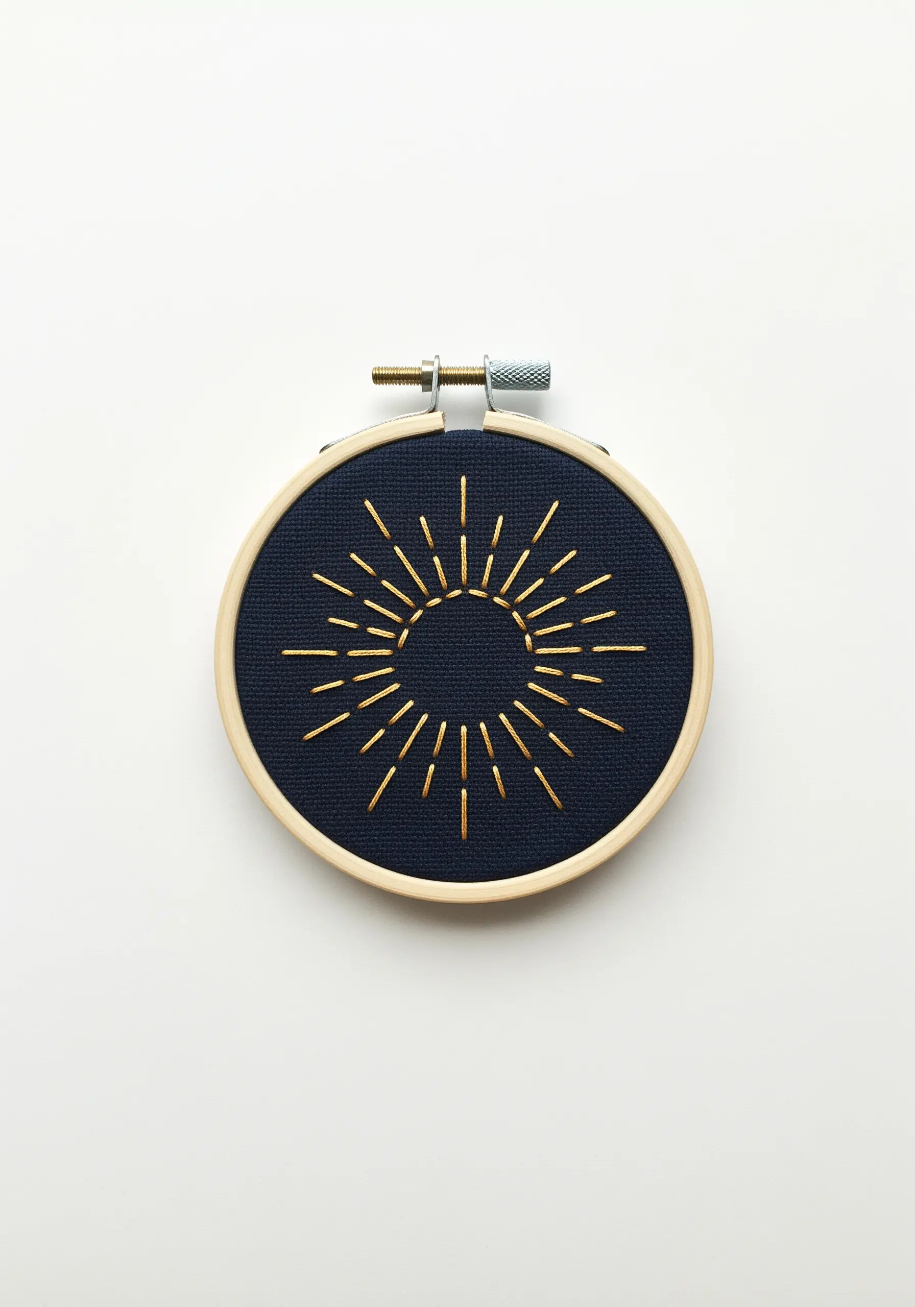 Gold thread sunburst embroidered with straight stitches on dark navy fabric.