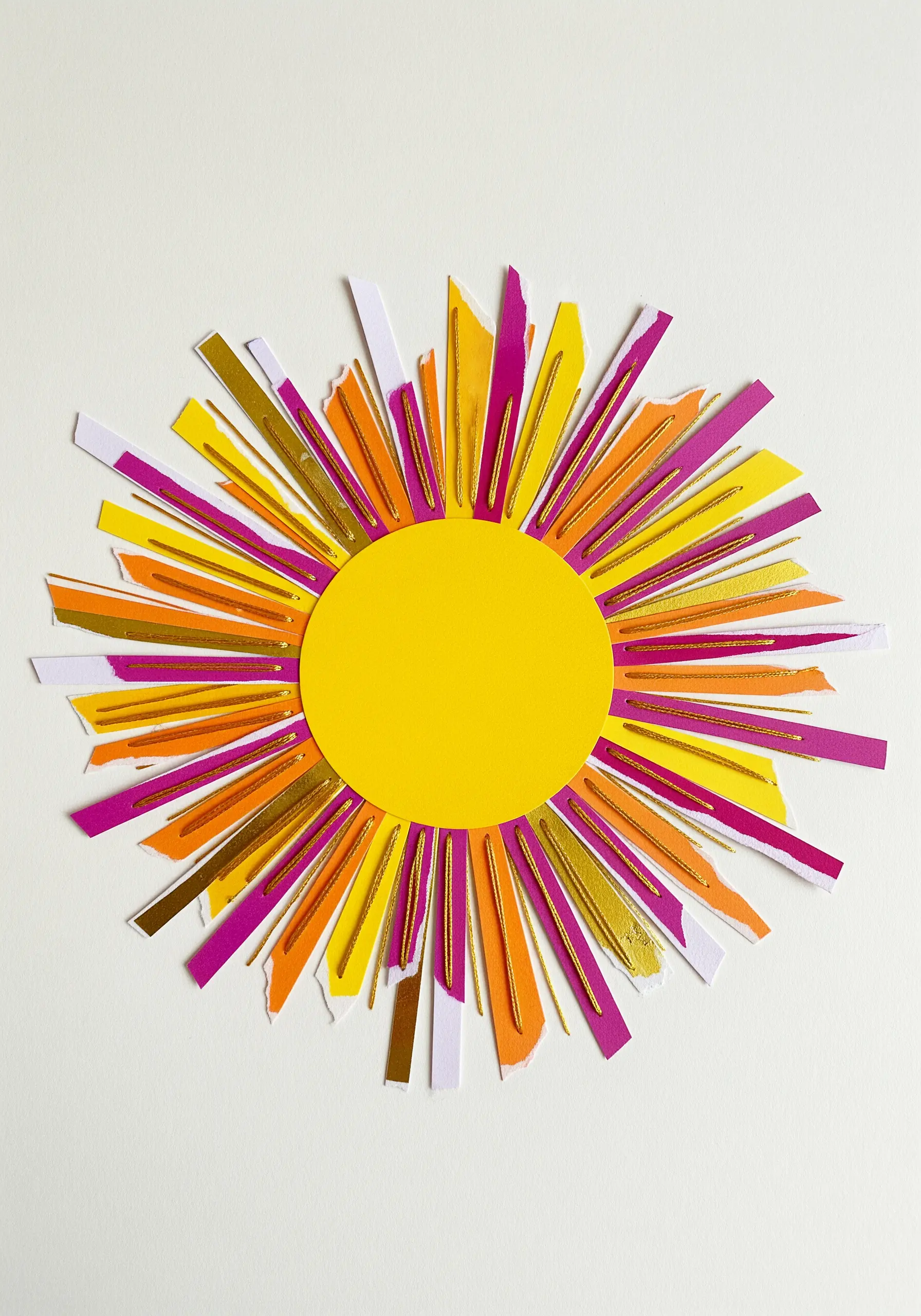 A sunburst collage made of colorful paper strips, with gold metallic thread stitched as rays.