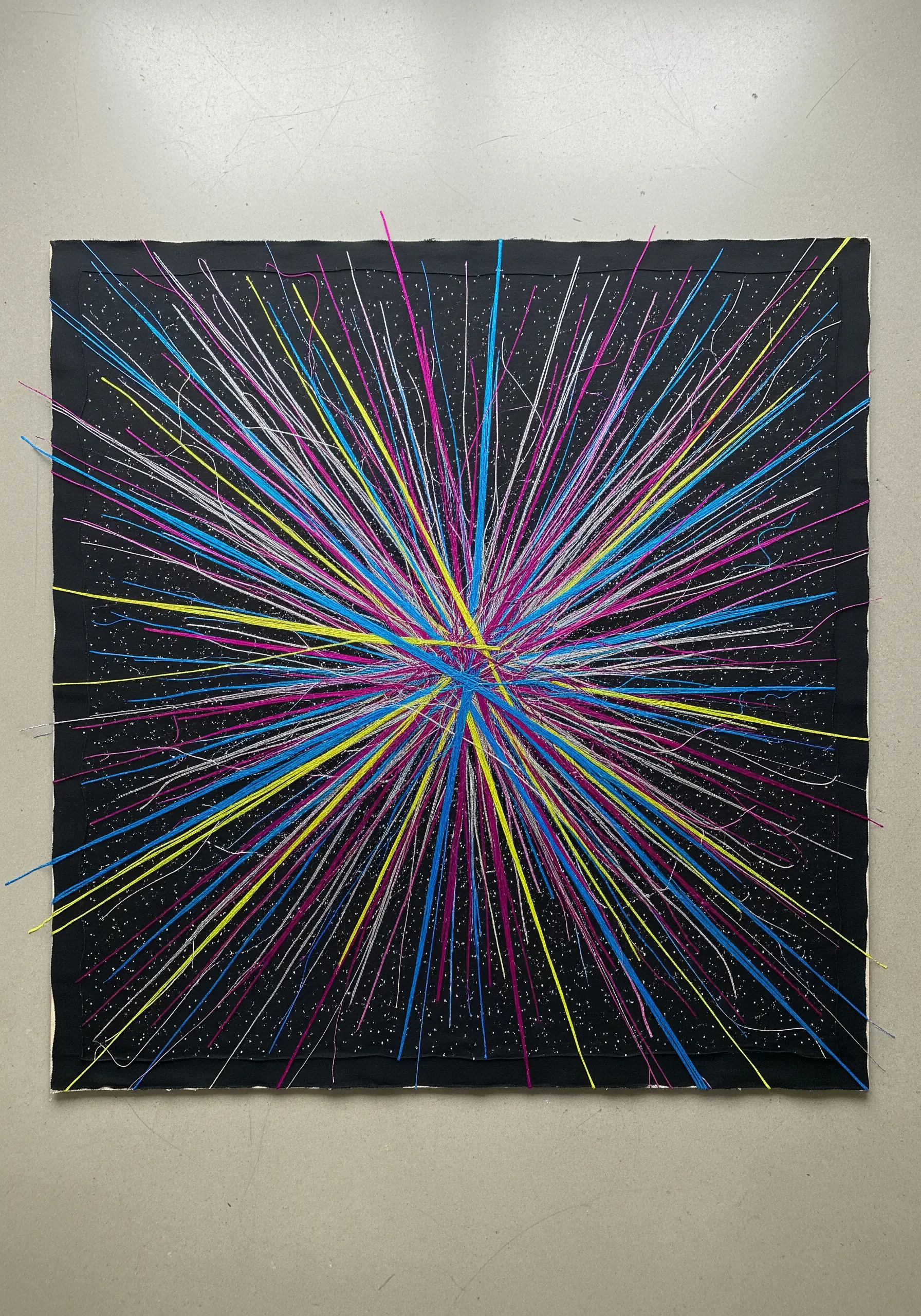 Abstract embroidery with radiating lines in pink, yellow, and blue on black fabric.