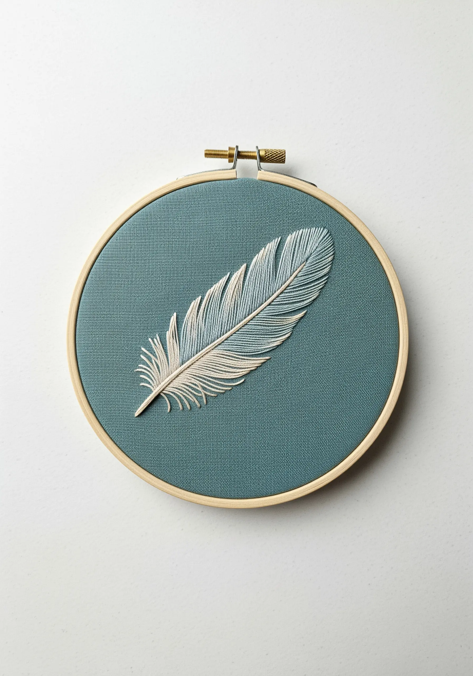 A delicate white and light blue feather embroidered on teal fabric.