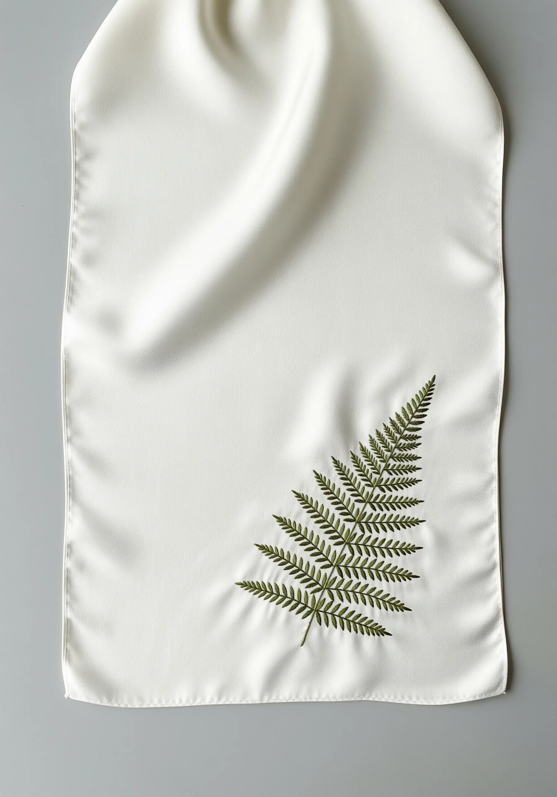 A realistic green embroidered fern frond on a white satin scarf.