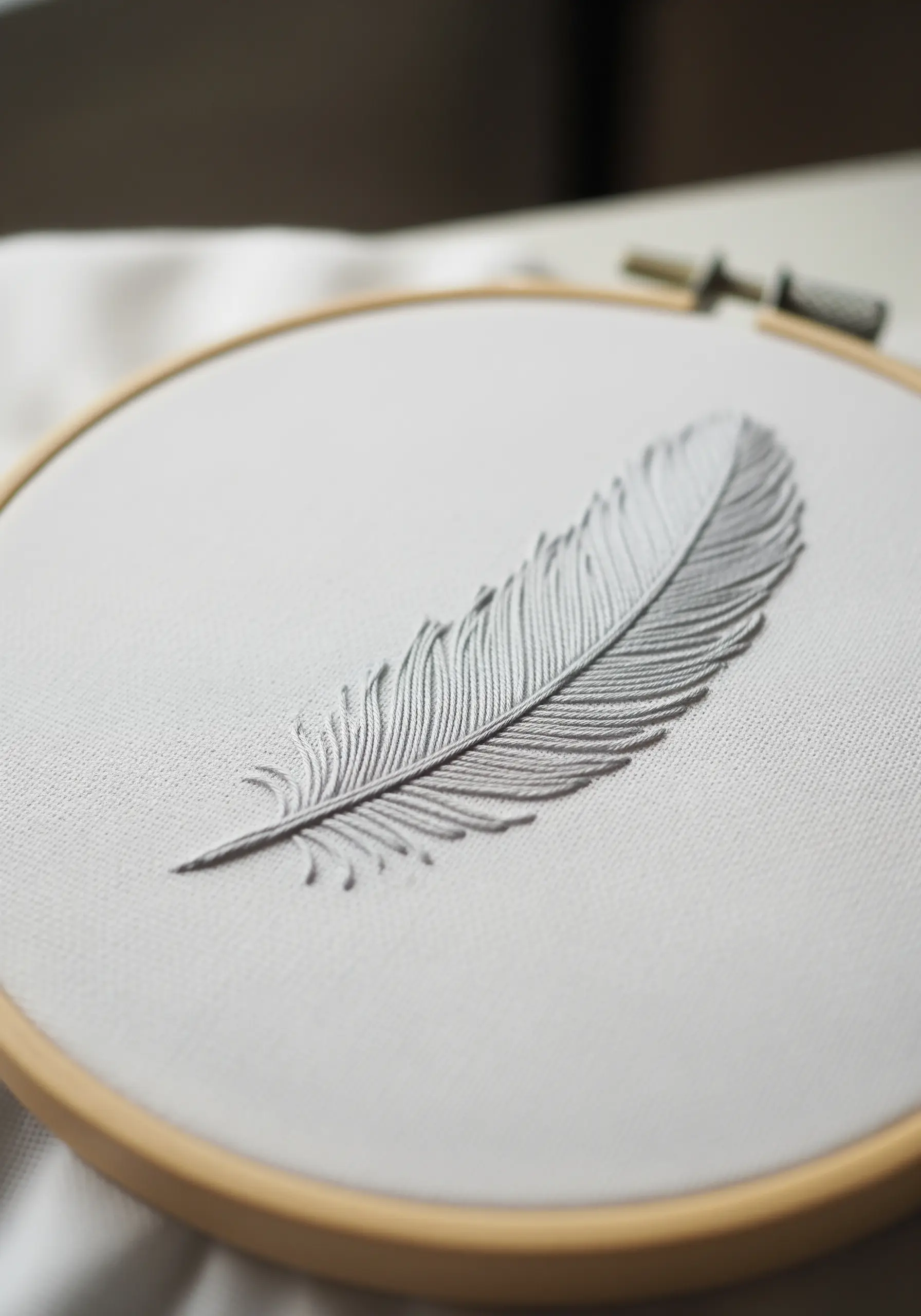 A delicate grey feather embroidered with fine fly stitches on a white canvas background.