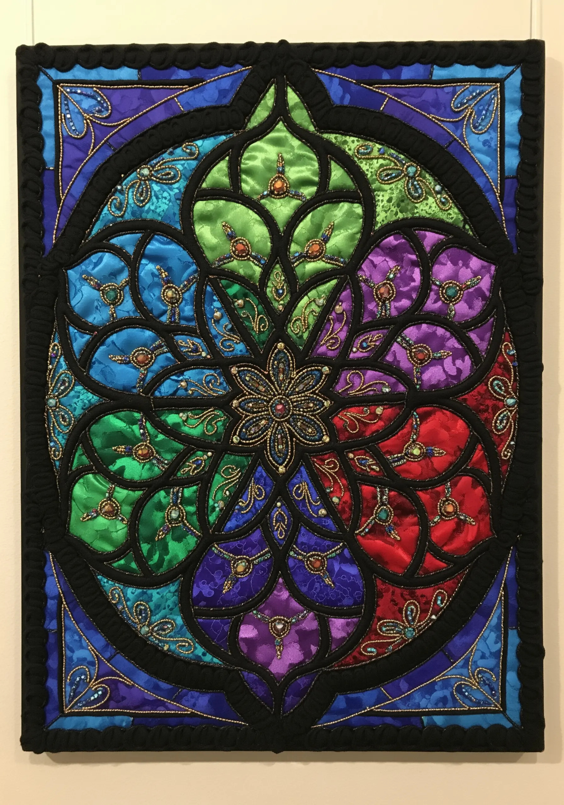 Fabric collage mandala in a stained glass style with jewel tones and heavy beadwork.