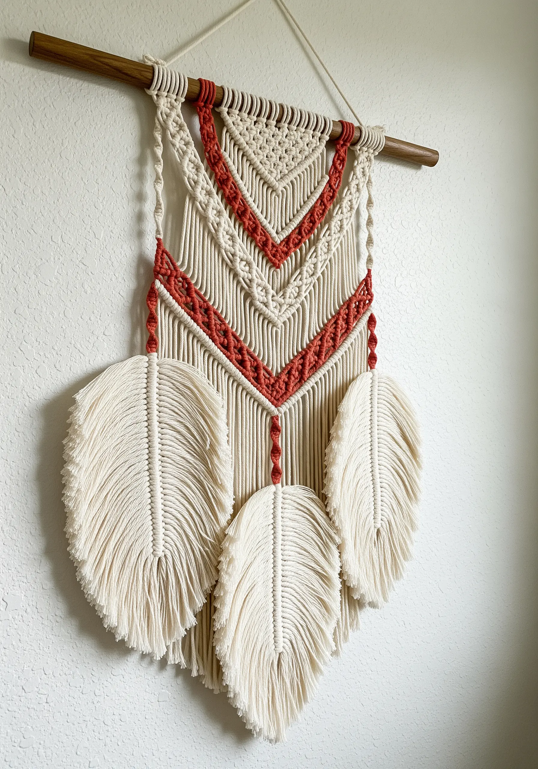 A natural and terracotta macrame wall hanging featuring three large, combed-out feathers.