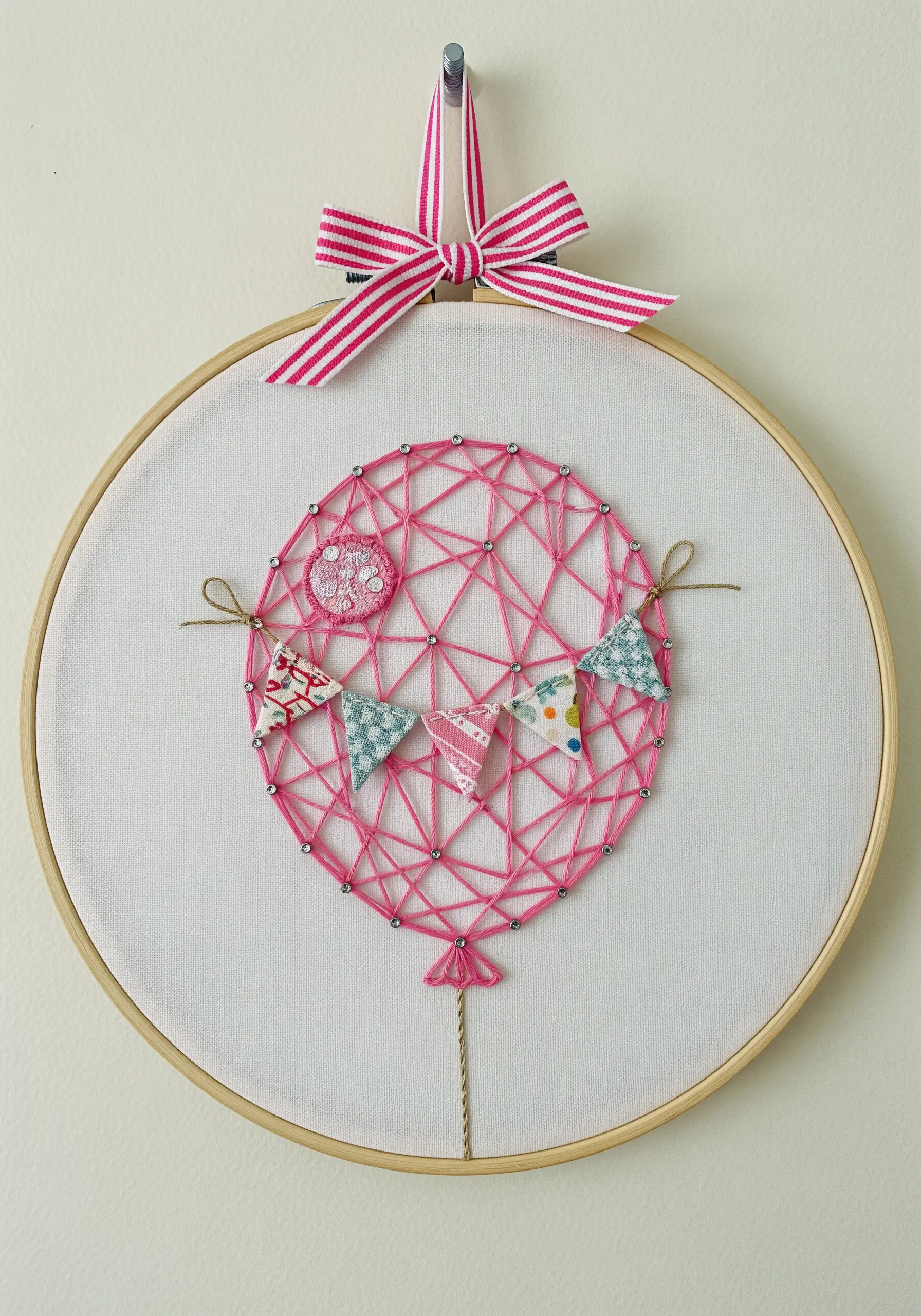 Pink string art balloon inside an embroidery hoop, decorated with a tiny fabric bunting.