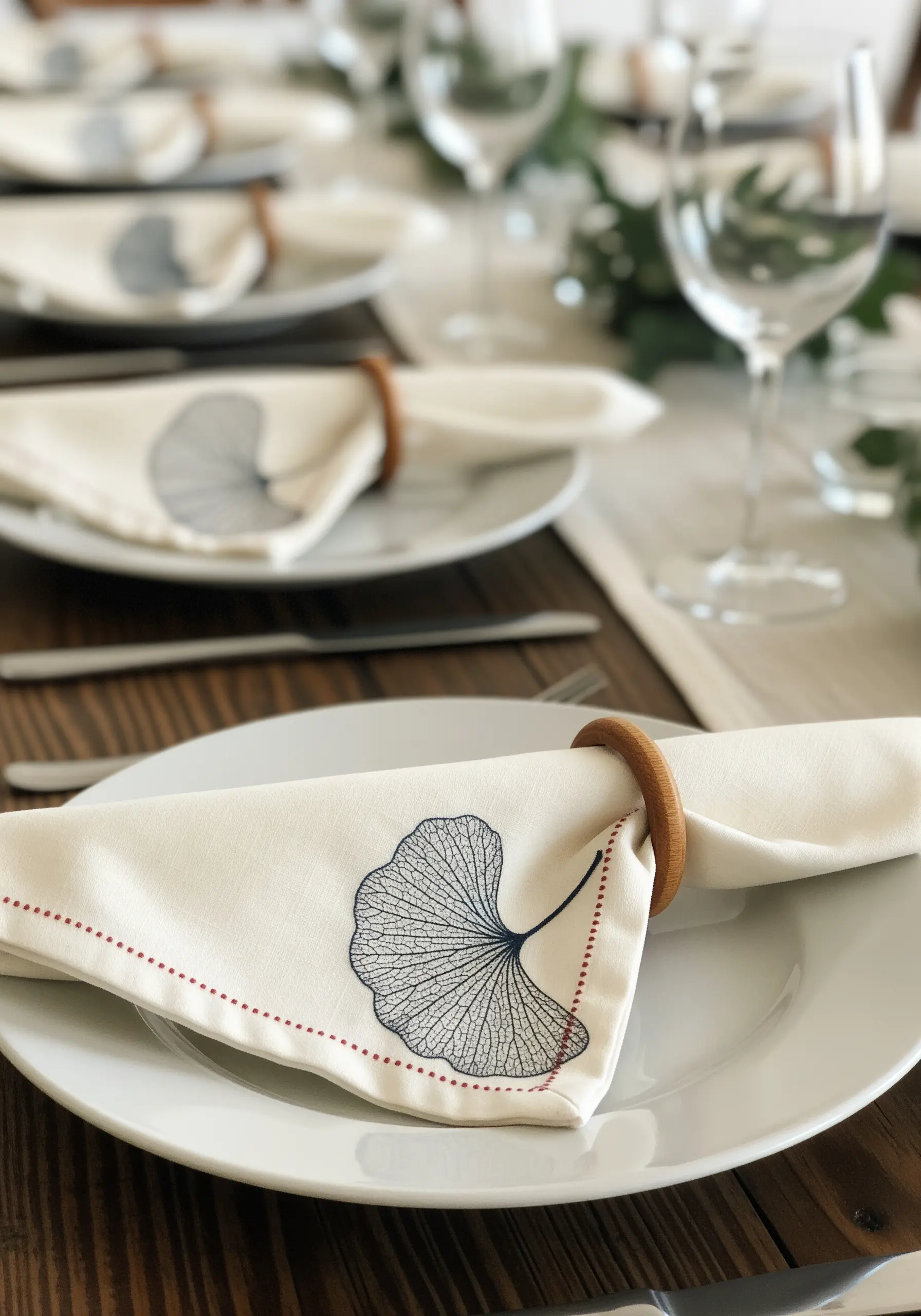 A white napkin with a finely embroidered ginkgo leaf showing delicate veins.