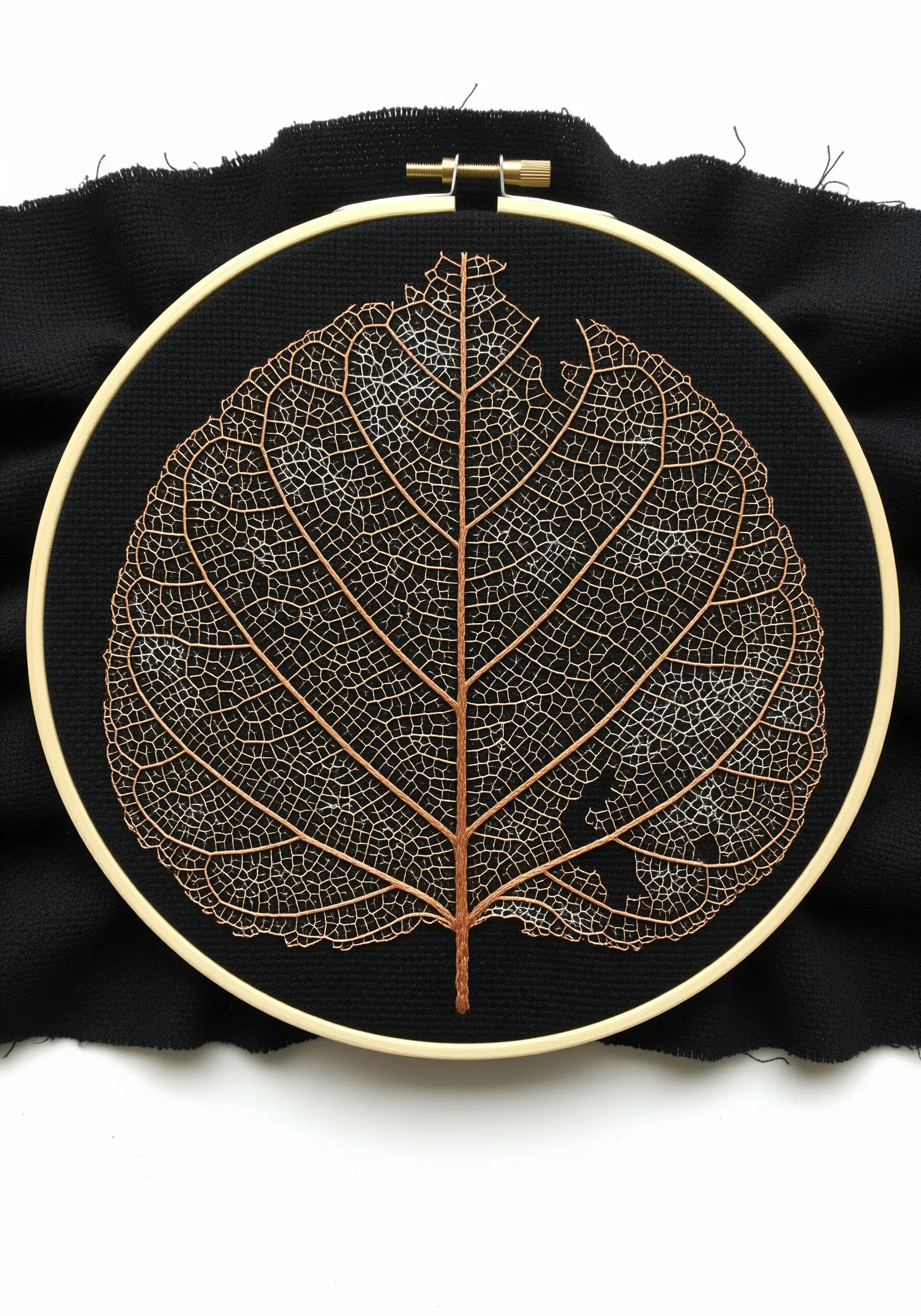 An intricate embroidery of a skeleton leaf using single-strand copper thread on black fabric.