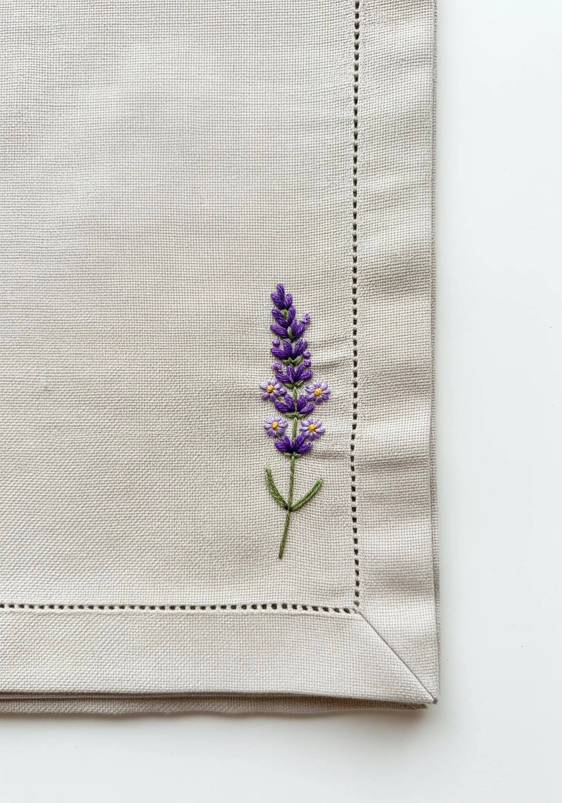 A single sprig of lavender embroidered on a neutral linen napkin.