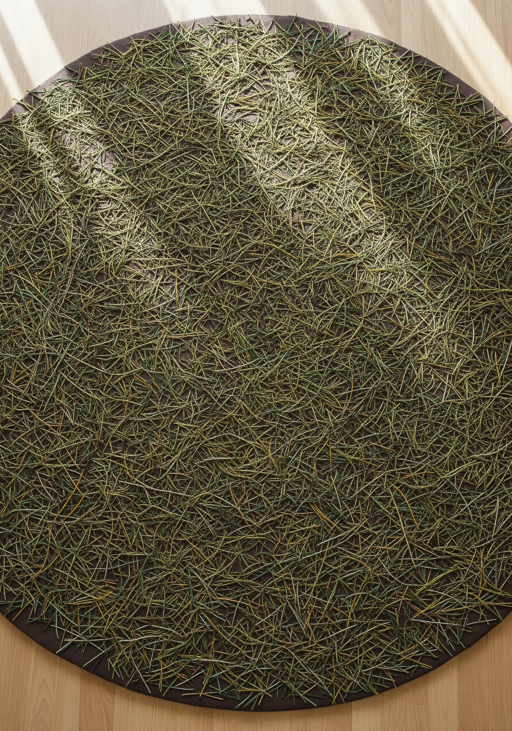 A circular textile piece covered in thousands of layered straight stitches resembling pine needles.