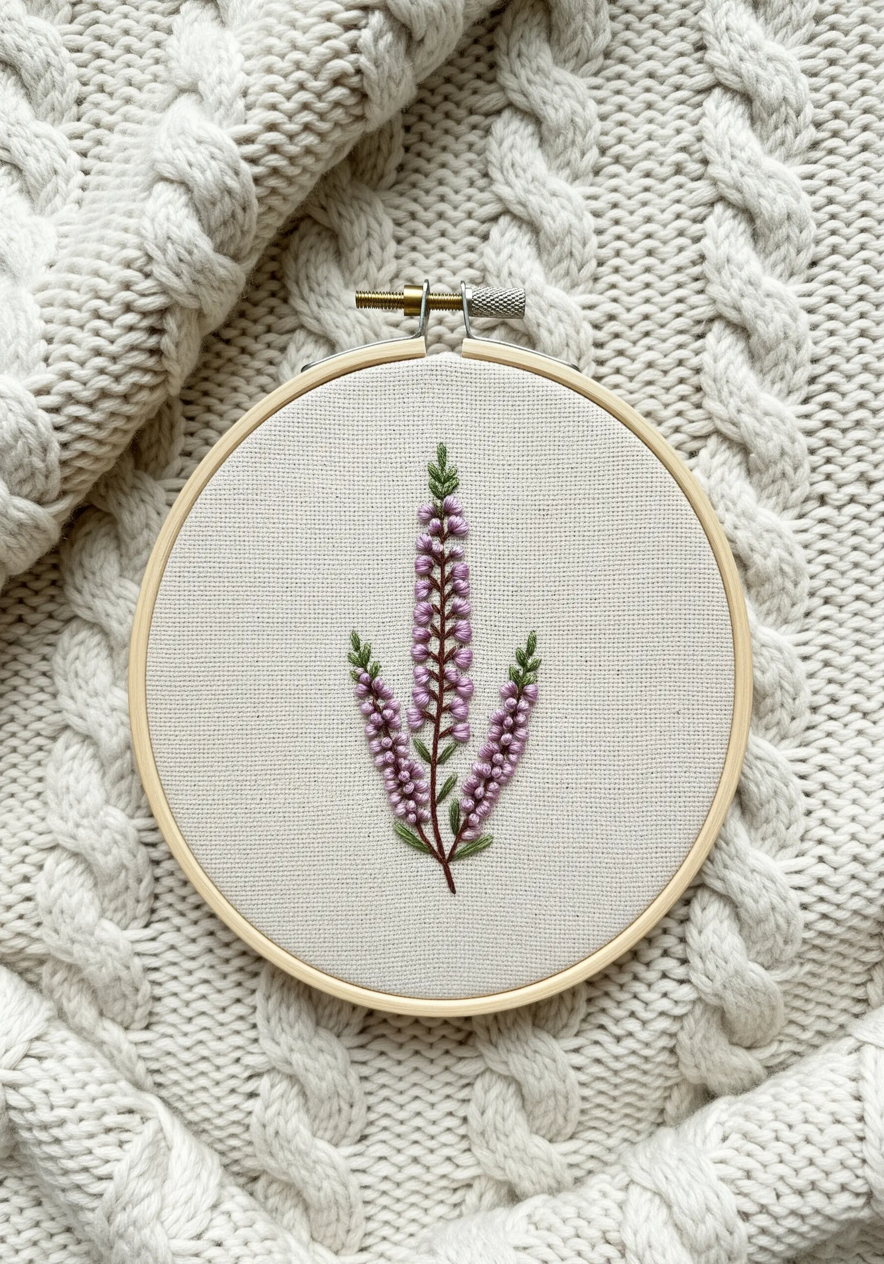 Embroidered heather sprigs with purple colonial knots on a cream fabric, laid on a knit sweater.