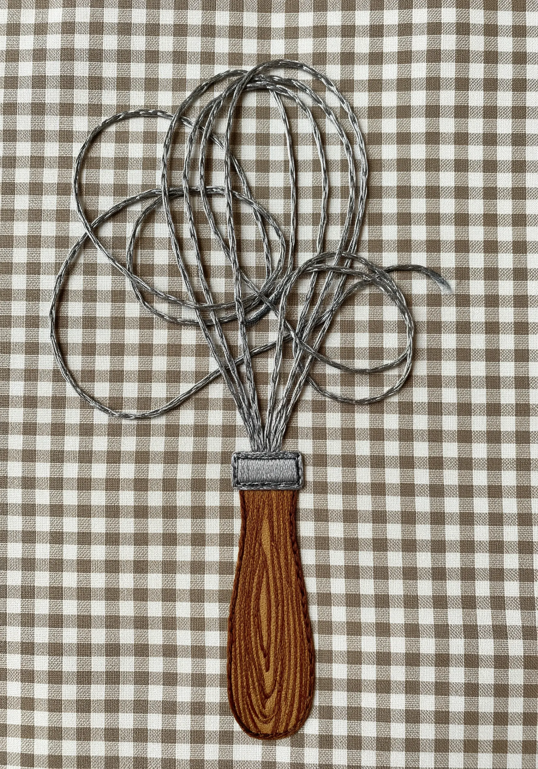 An embroidered whisk with a realistic wooden handle on a gingham background.