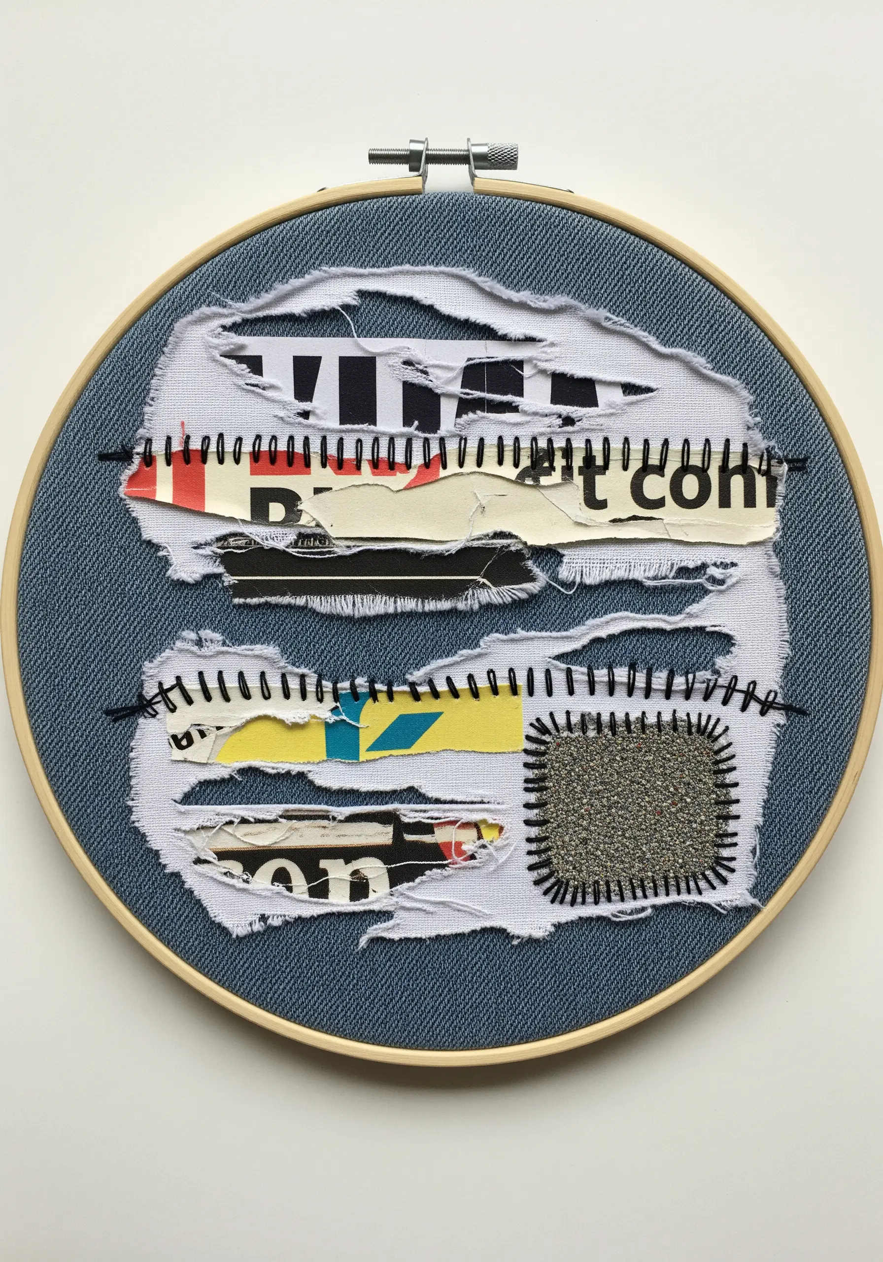 Torn denim fabric revealing magazine paper scraps underneath, framed with black stitches.