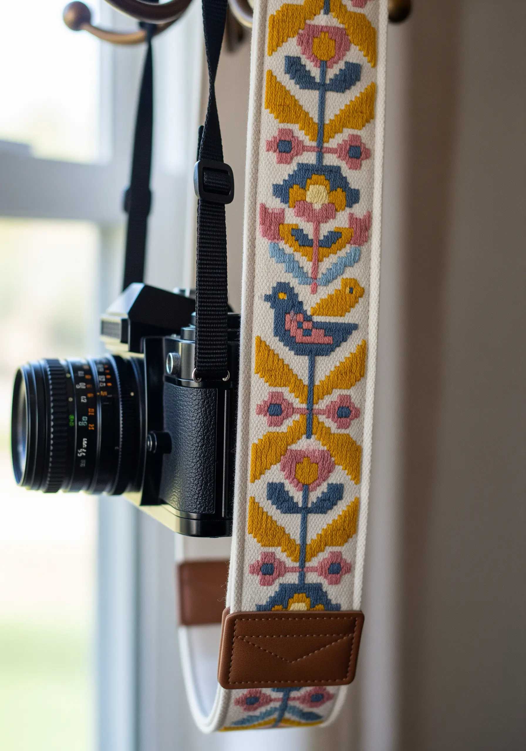 A woven camera strap with a Scandinavian-inspired folk art pattern of birds and flowers.