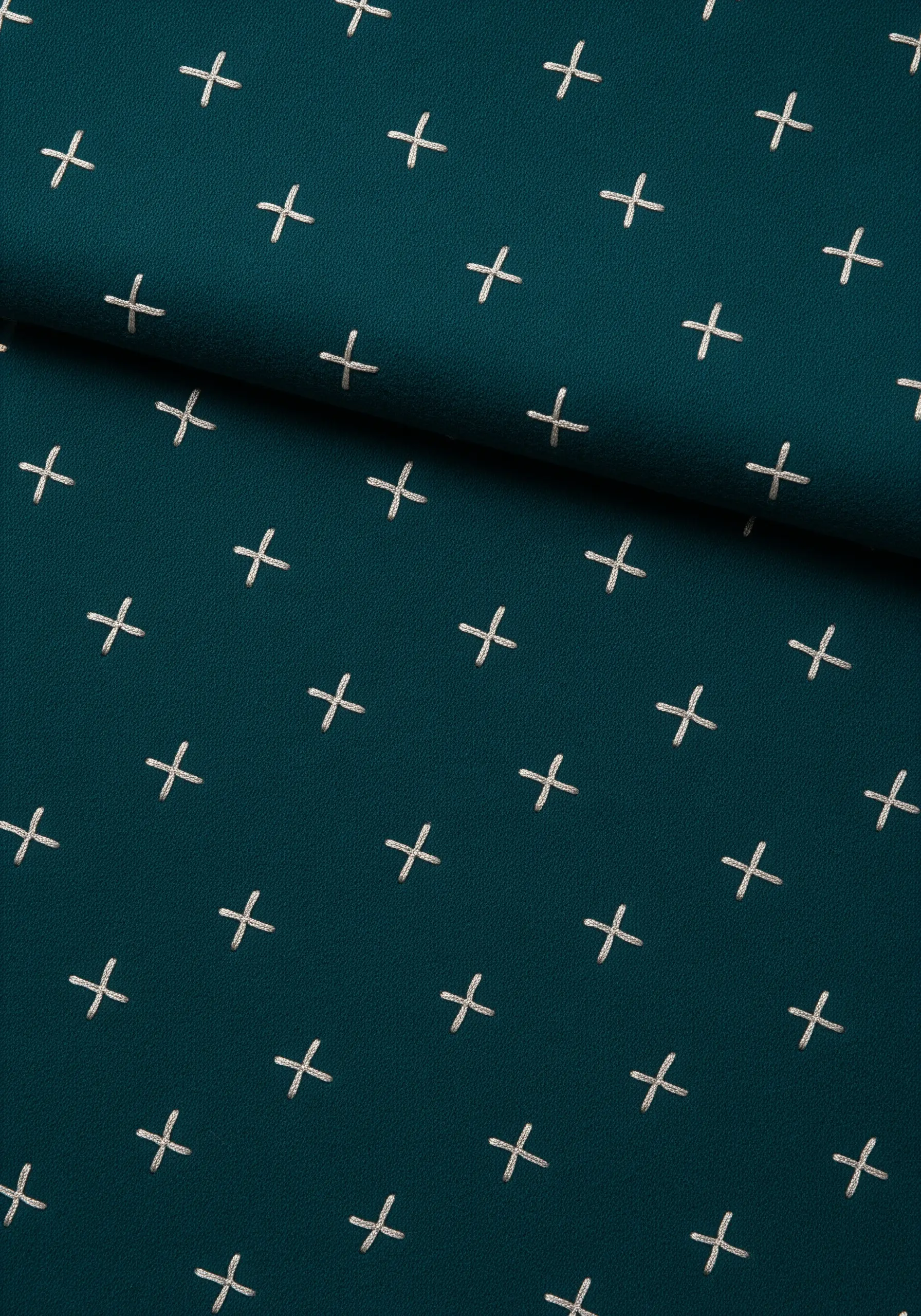 A repeating pattern of small white cross stitches on a dark teal scarf.
