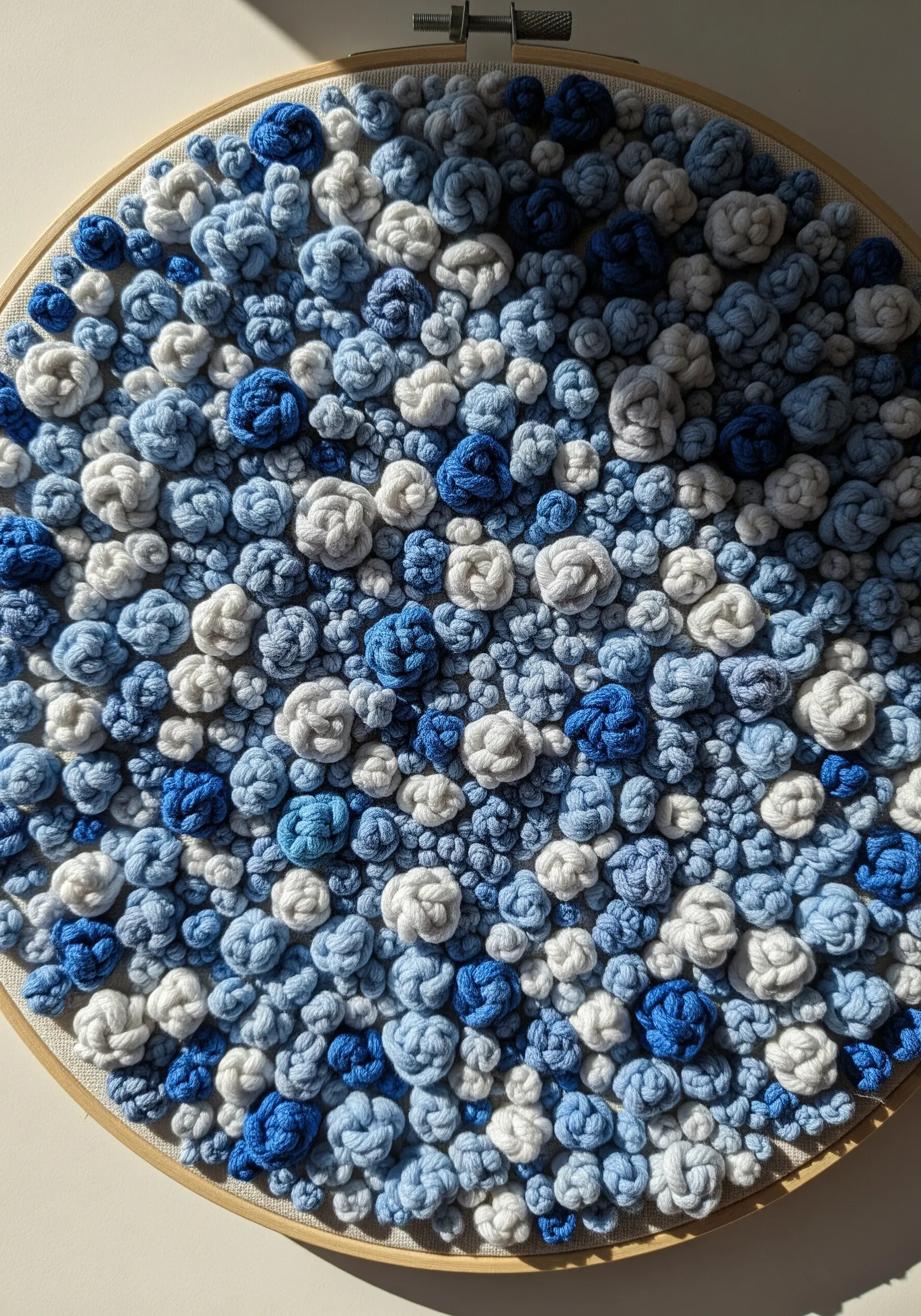 A dense, abstract collection of French knots in varying shades of blue and white filling a hoop.