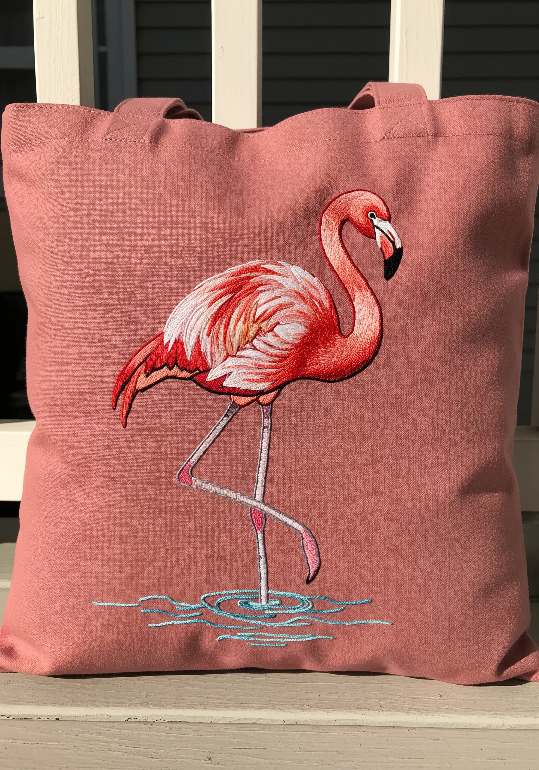 A detailed flamingo embroidered on a dusty pink tote bag, with thread-painted feathers.