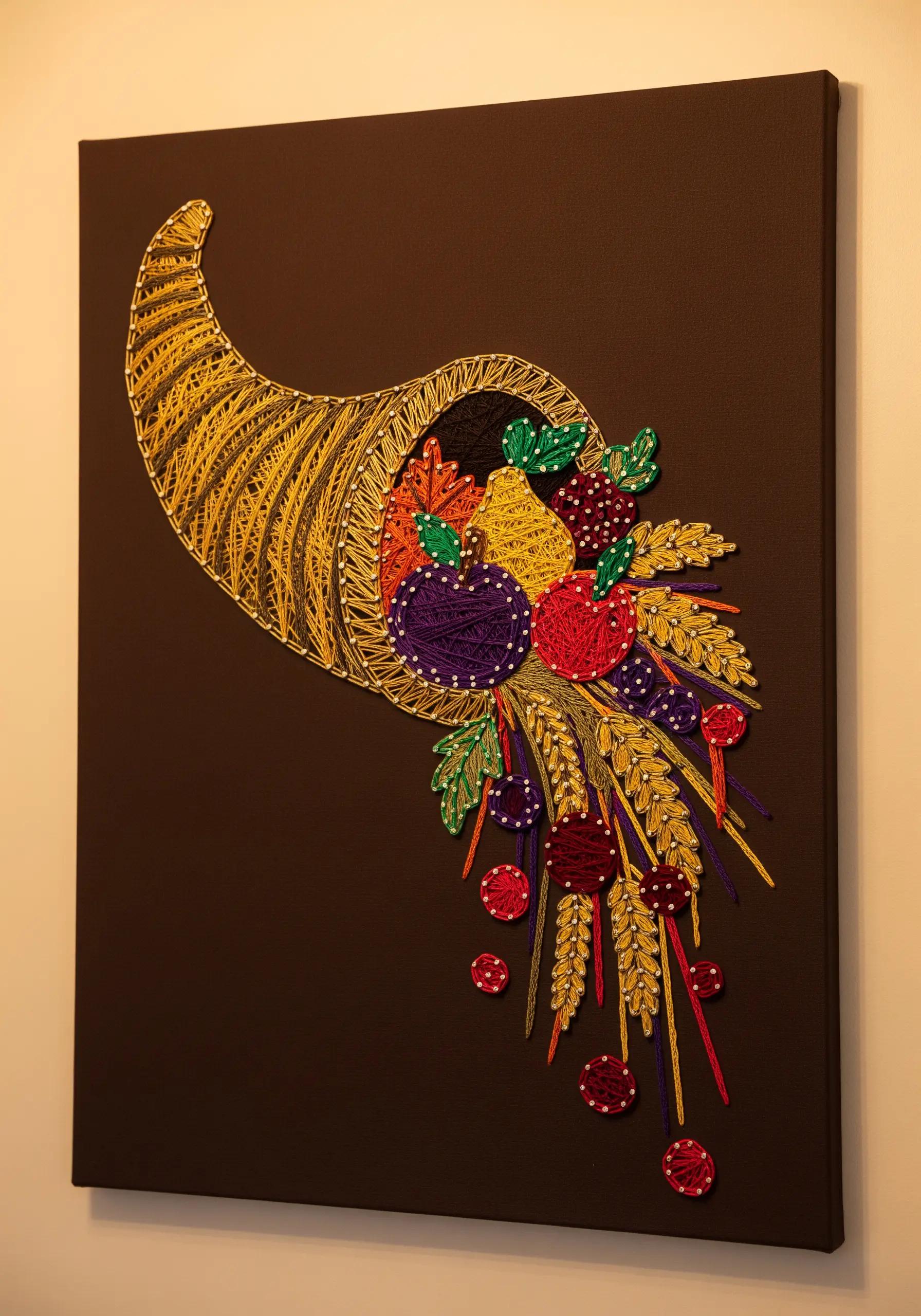 Colorful string art cornucopia with layered fruits on a brown canvas.