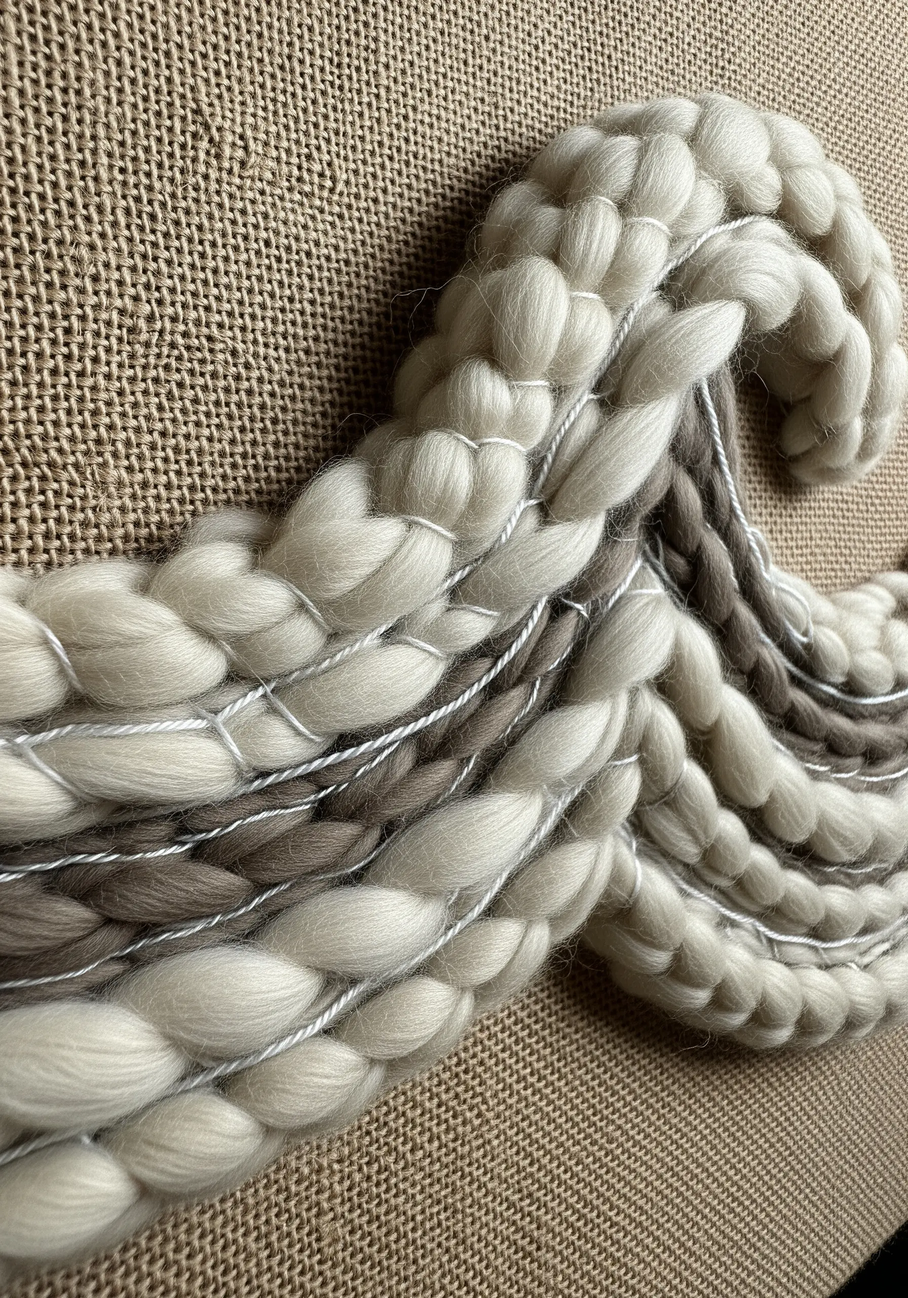 A thick wave made of chunky white and brown wool on a burlap canvas.
