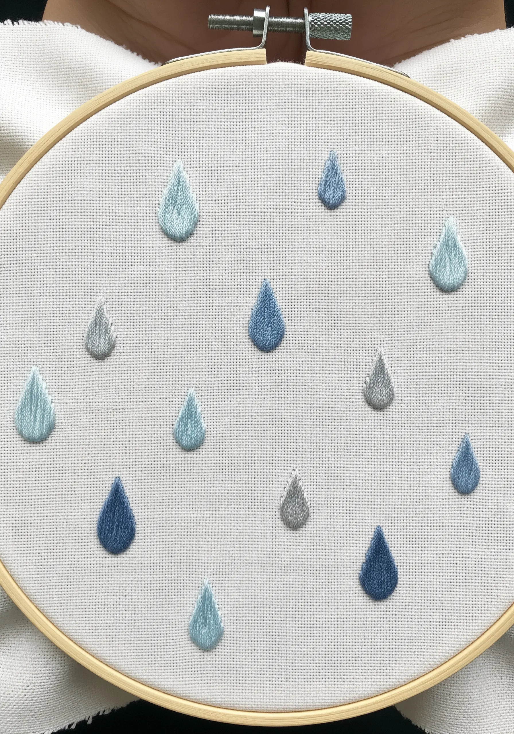 Padded satin stitch raindrops in various shades of blue and gray.